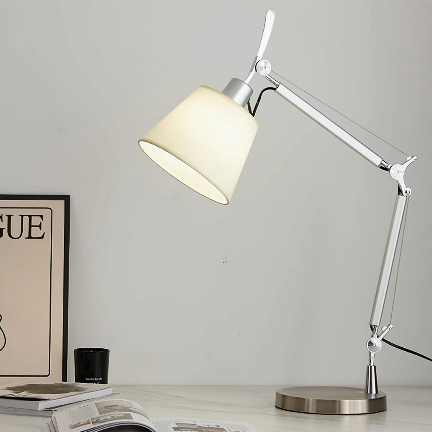 Warm-lit adjustable table lamp in home office ambiance, creating focused task lighting over desk with publications and decor