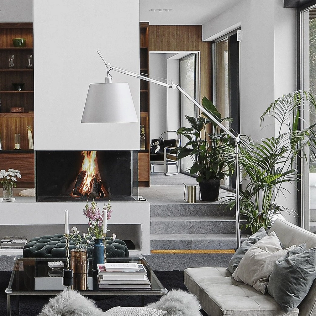Adjustable swing arm floor lamp beside fireplace lounge with green plants, silver metal frame and white fabric shade