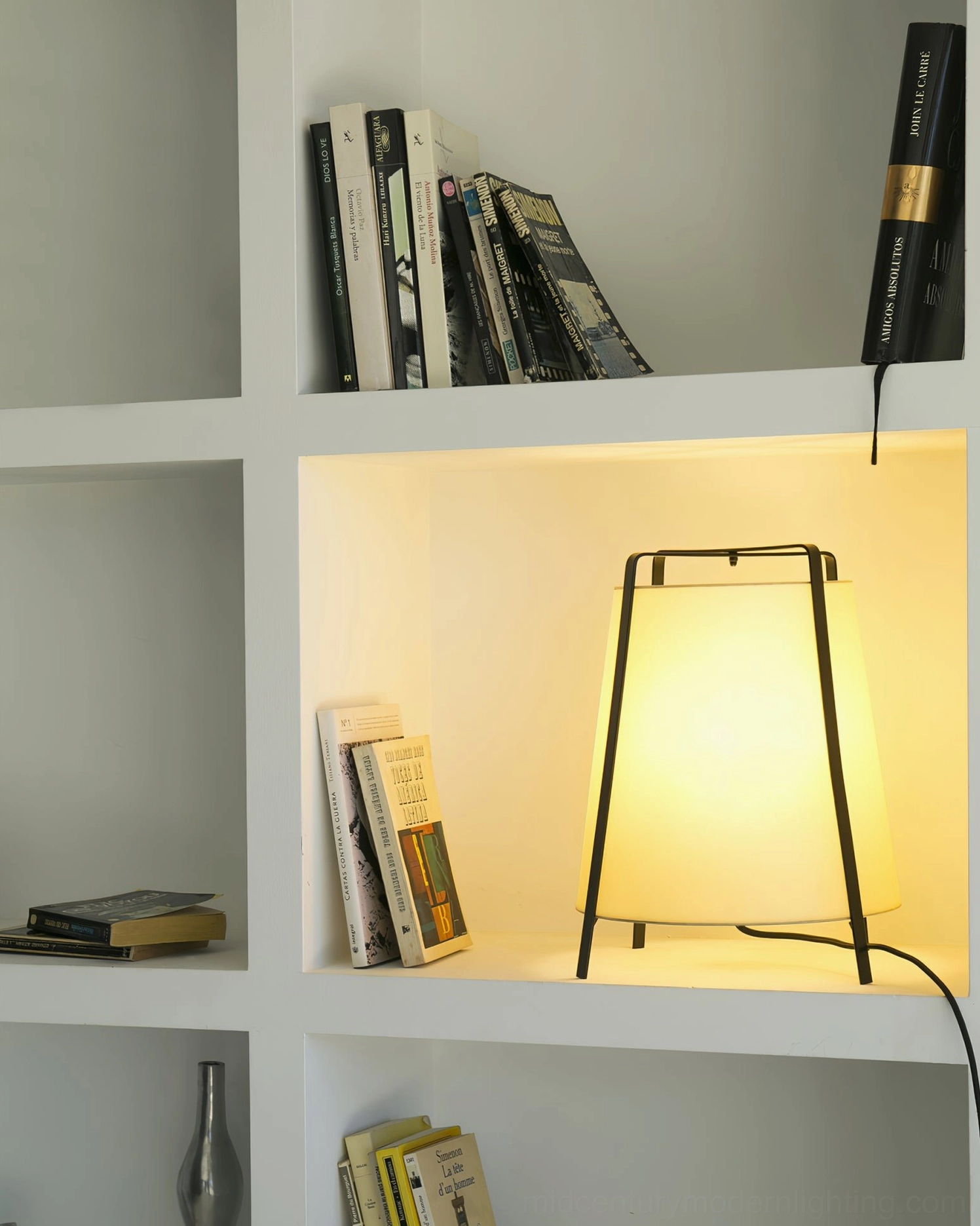 Akane table lamp illuminated inside built-in bookshelf niche, black metal stand creating modern accent lighting