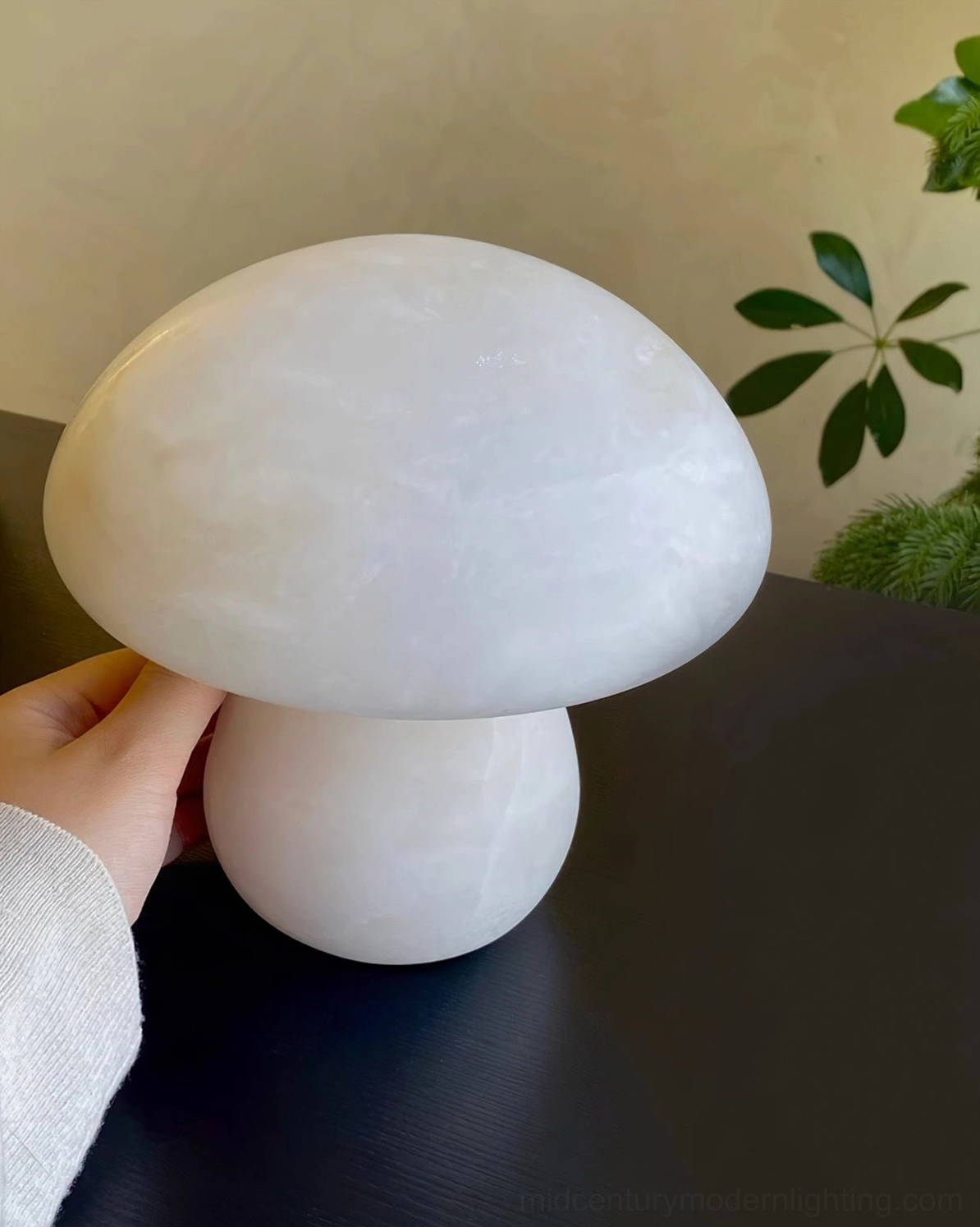 Tactile smooth alabaster mushroom lamp held by human hand showing texture detail and warm off-white tone