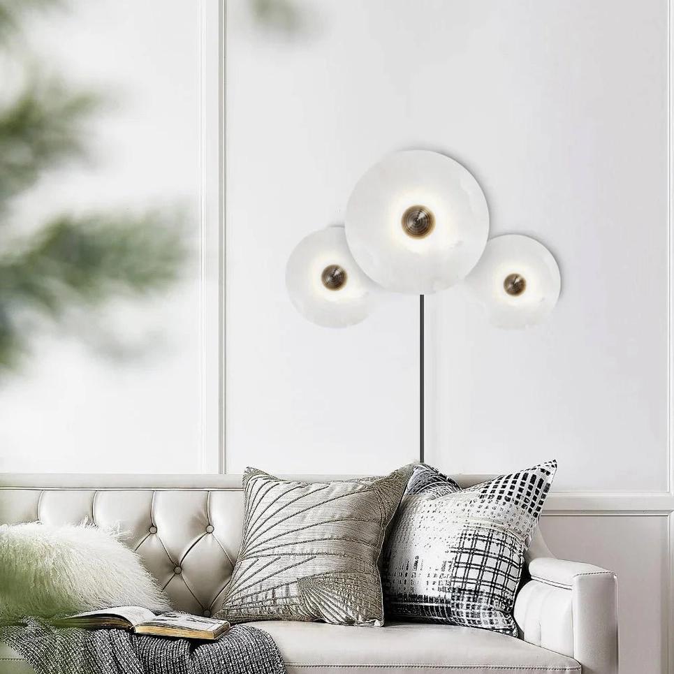 Close-up detail of alabaster wall lamp illuminating tufted sofa and neutral throw pillow styling
