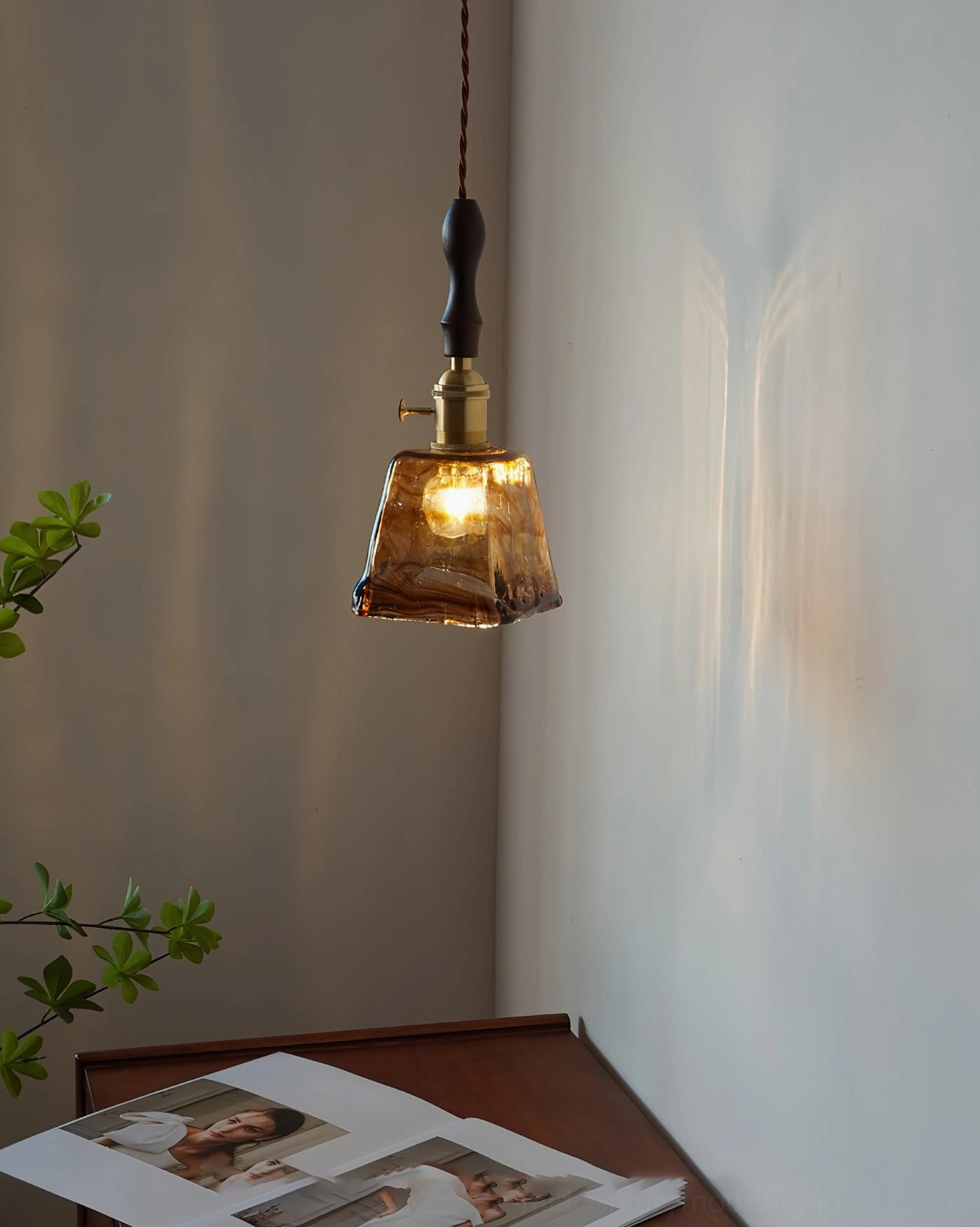 Marbled amber glass pendant casting warm light in sunlit residential desk corner with magazines and green foliage