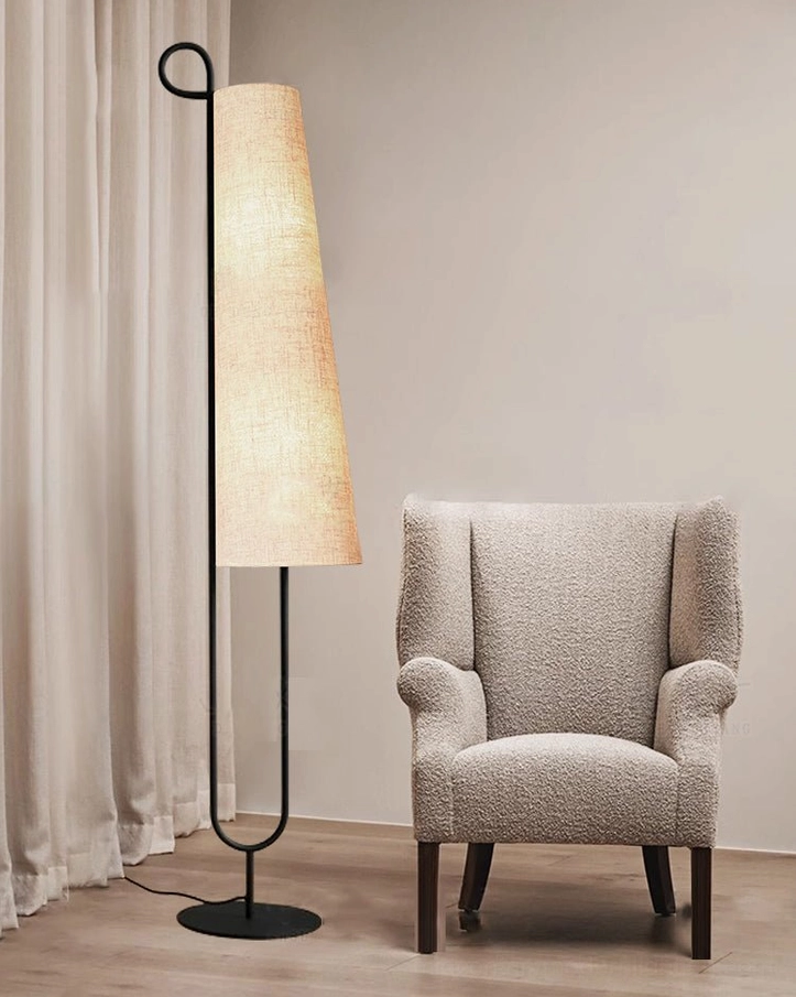 Sleek Ancora floor lamp with black metal stand and glowing fabric shade beside boucle armchair and sheer curtain