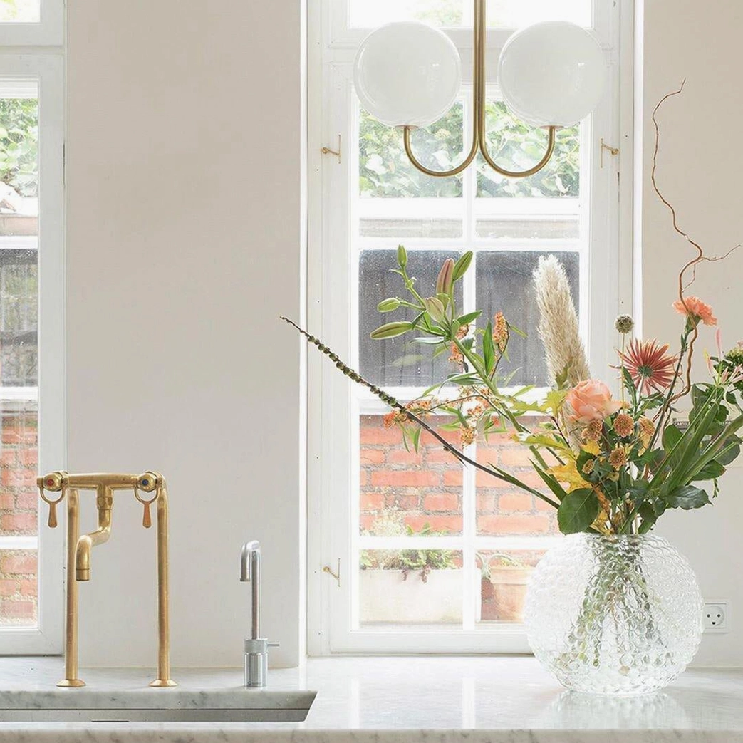 Double globe pendant chandelier in bright kitchen with marble countertop and decorative floral arrangement