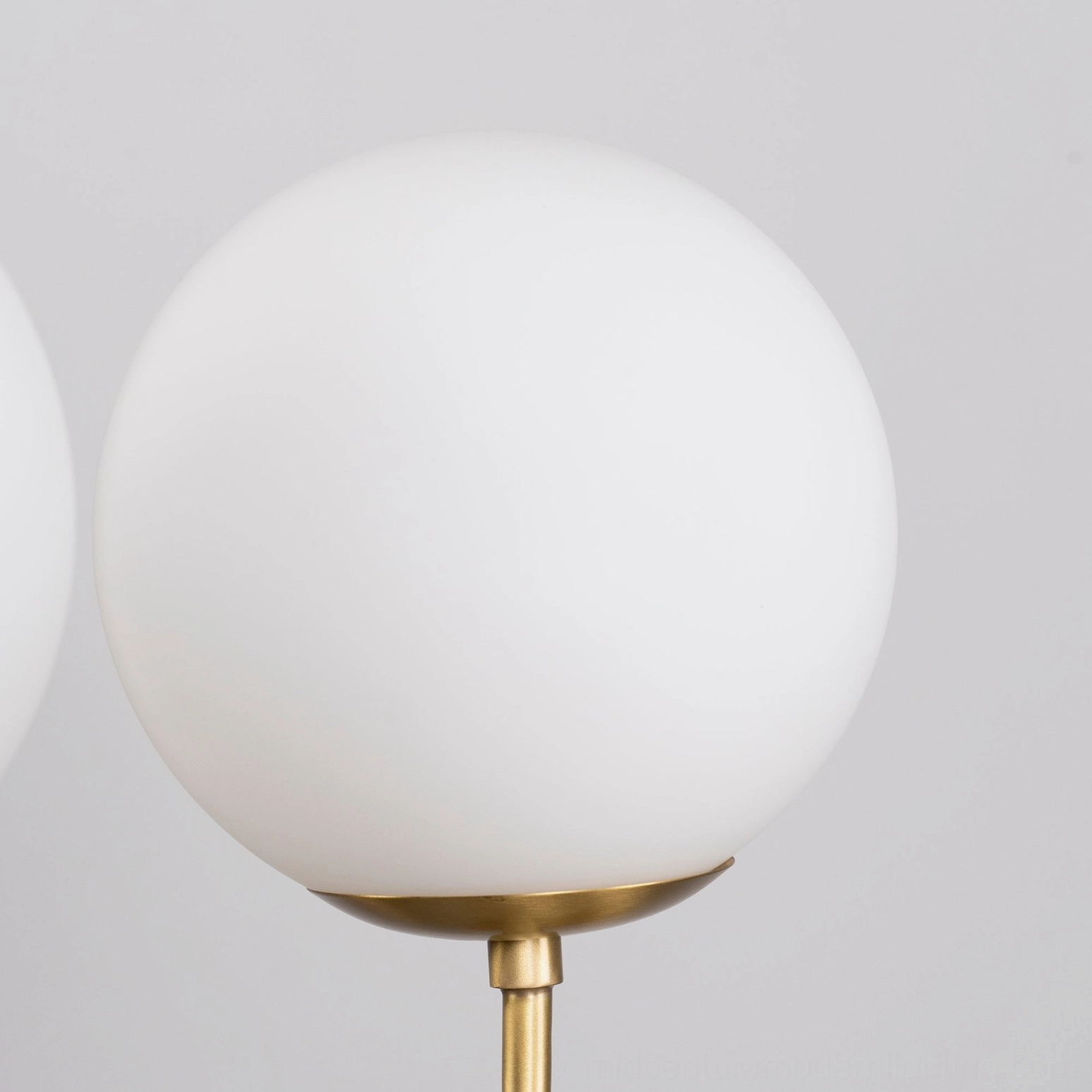 Side view of single frosted white glass globe with brass gold mounting base on light gray background