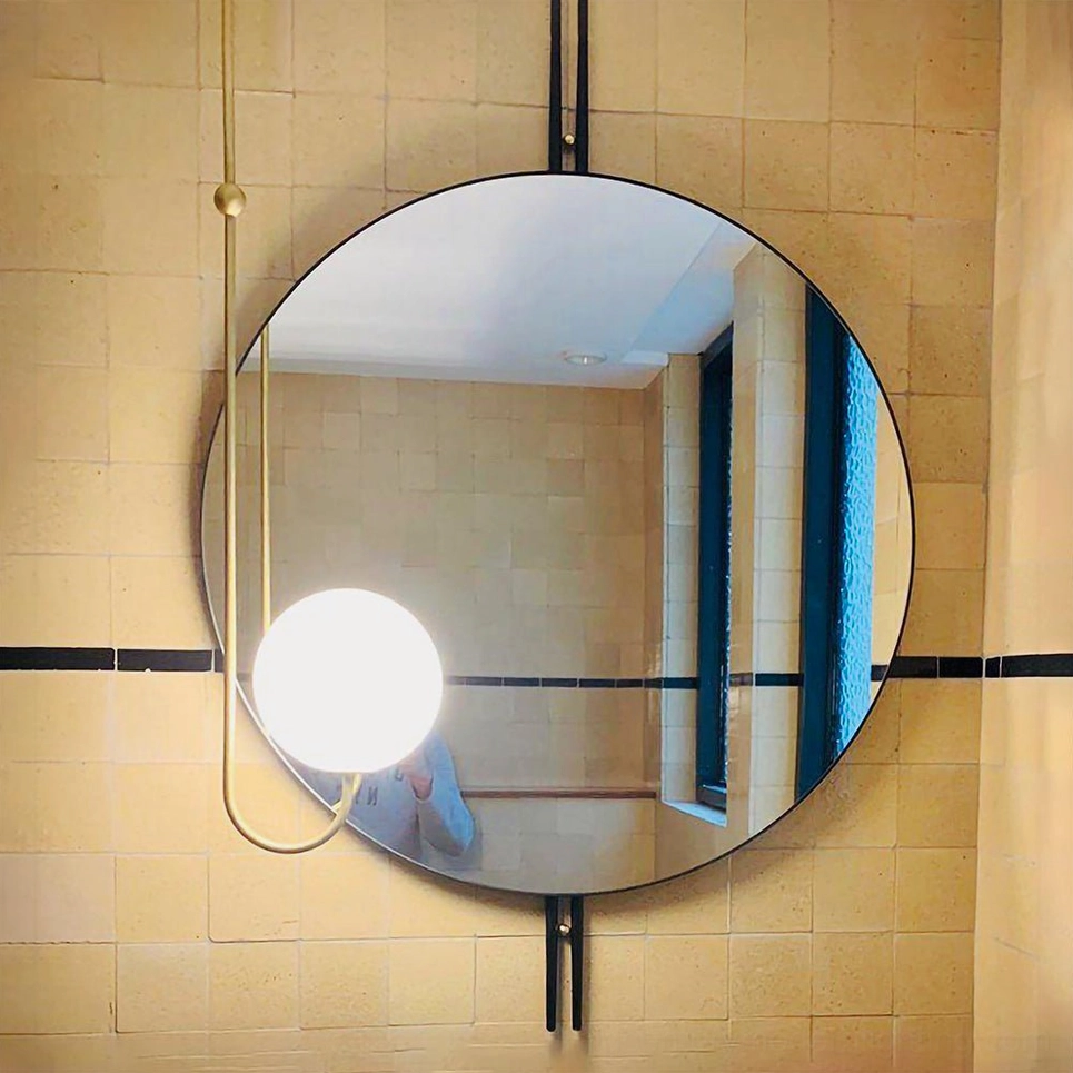 Single globe wall sconce with brass curved arm and frosted white glass shade in yellow tiled bathroom