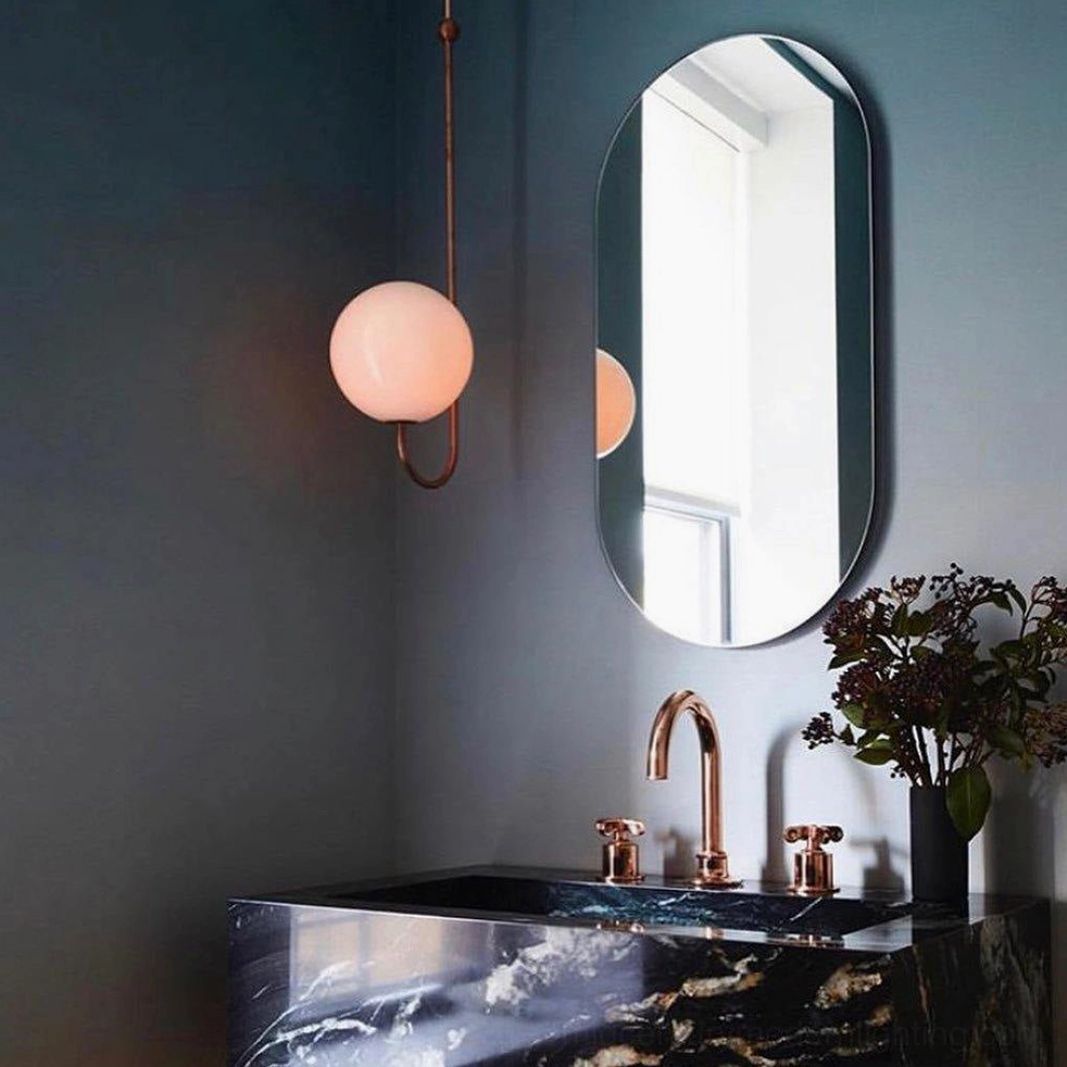 Single frosted glass globe wall sconce with copper brass hardware in luxury dark blue bathroom