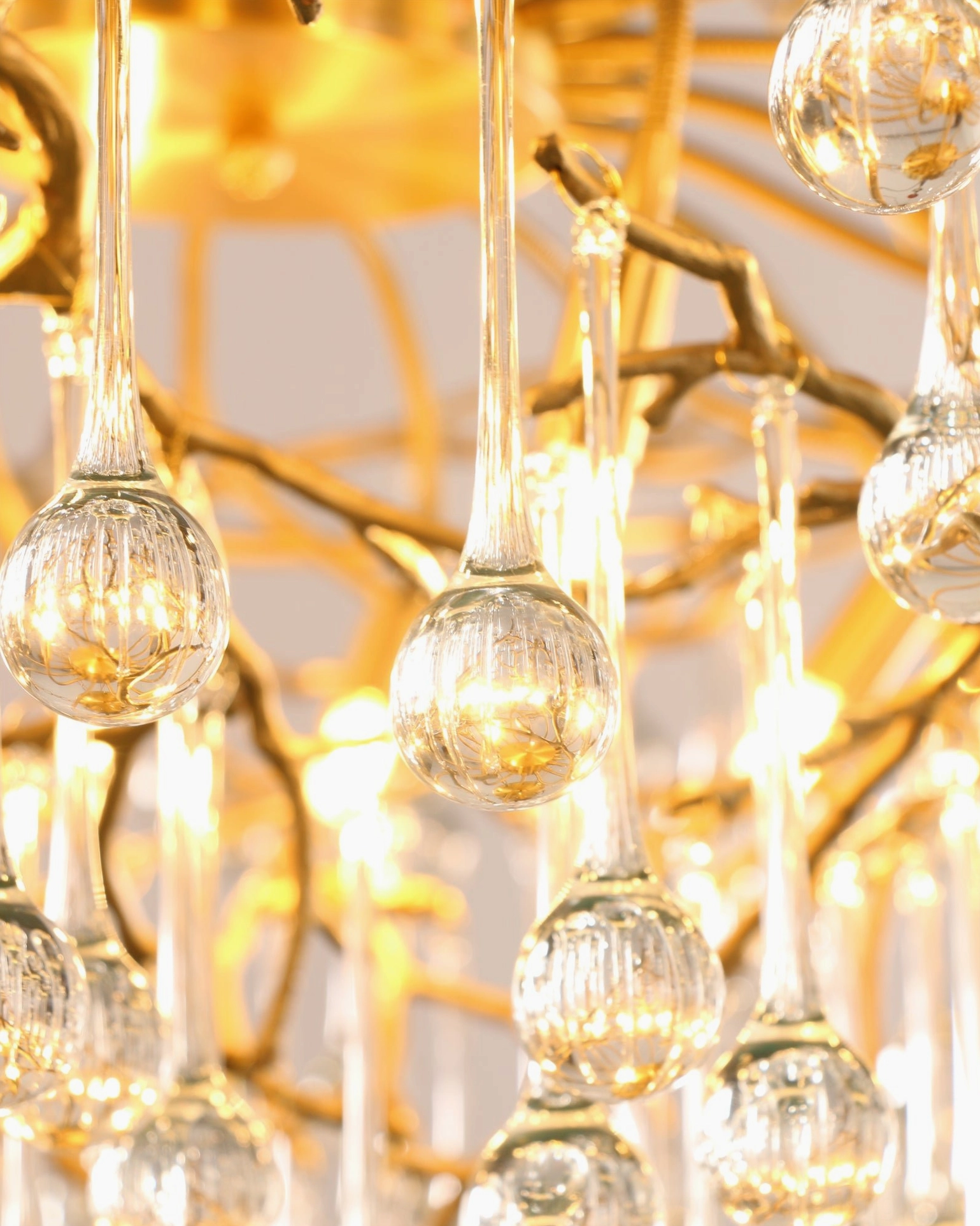Illuminated Anita crystal chandelier with glowing glass droplets and polished gold framework