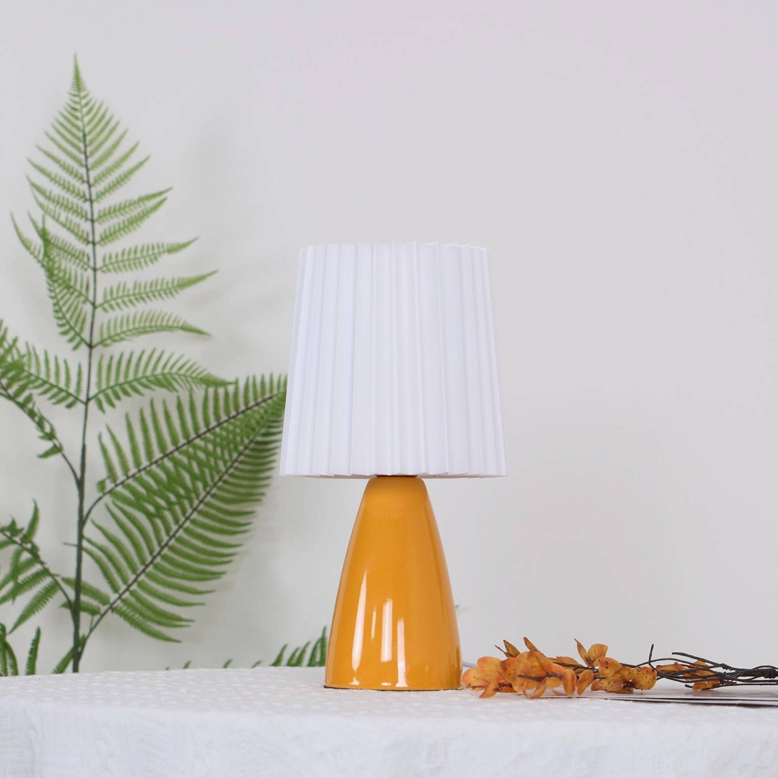 Apollo table lamp with fern decor on table, white pleated shade and orange base