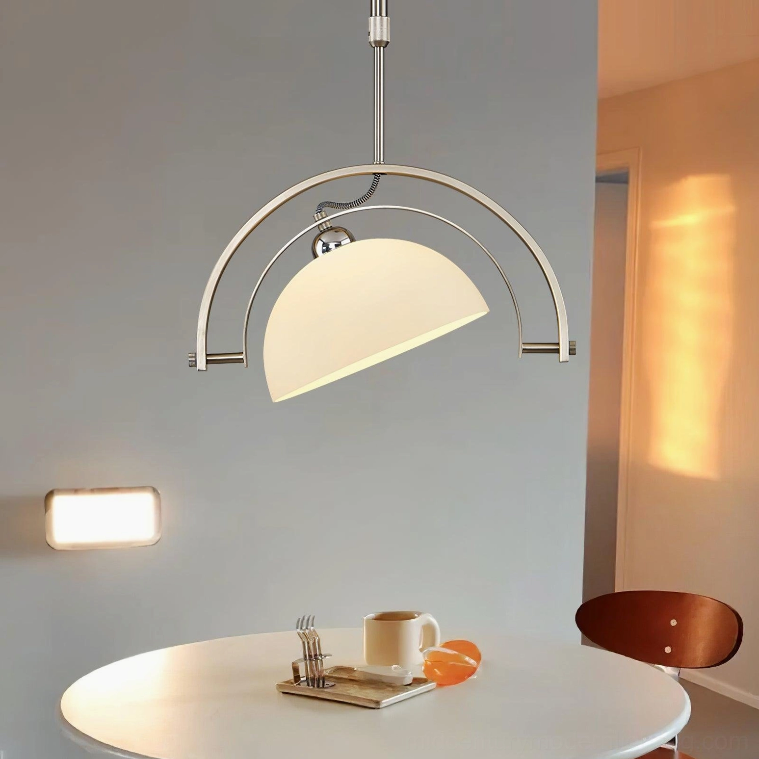 Arc pendant lamp mounted above white dining table in minimalist contemporary dining area with tableware setup