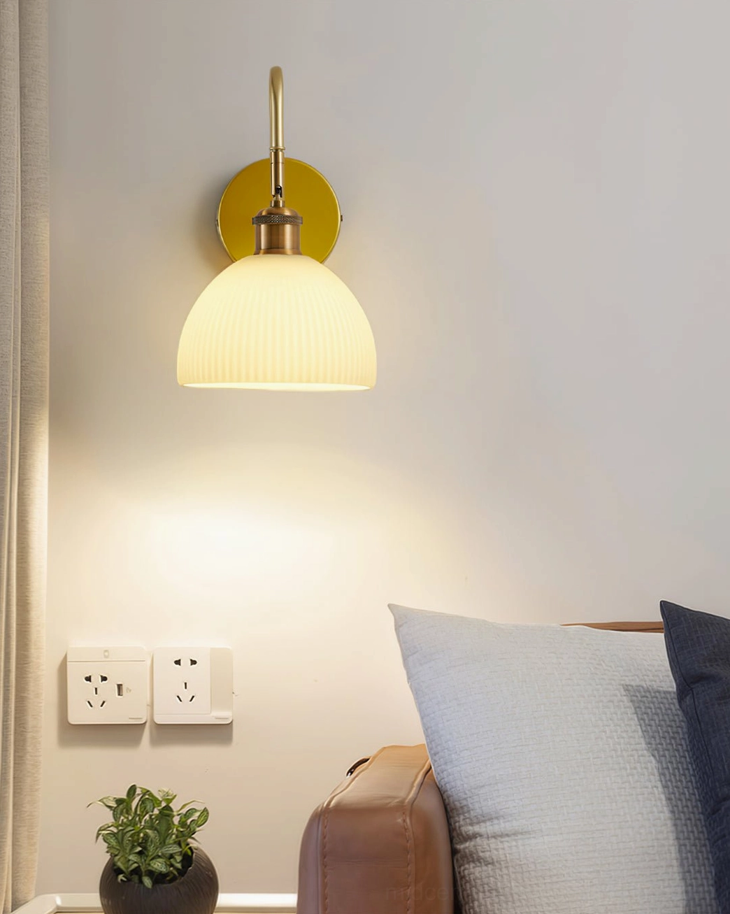 Arren accent wall lamp with solid brass round base and ribbed dome shade near living room sofa and plant
