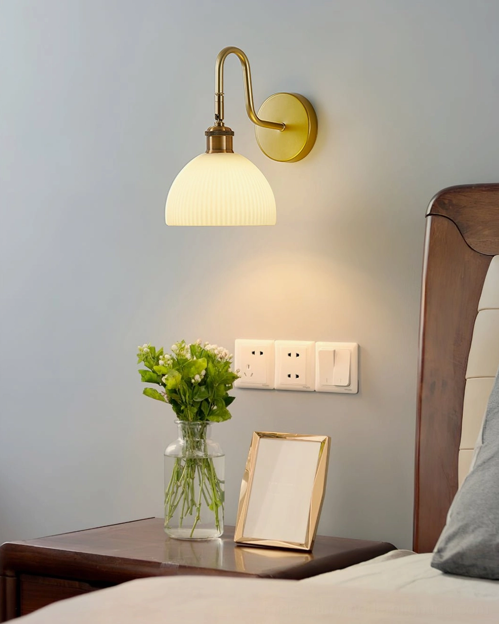 Arren bedside wall sconce with ribbed warm white shade and brass gold mount beside wooden bed frame