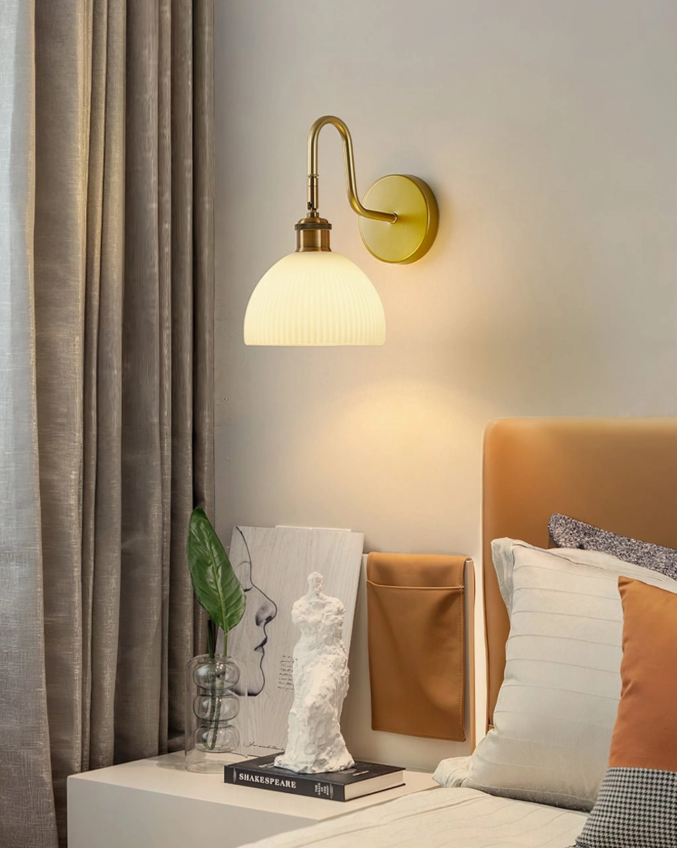 Modern Arren bedroom wall lamp with curved brass arm in bedroom with leather headboard and home accessories