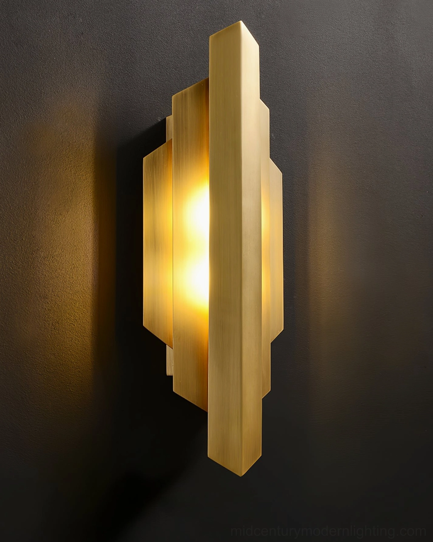 Close-up angled view of polished brass Art Deco wall lamp showing geometric layered design and warm light
