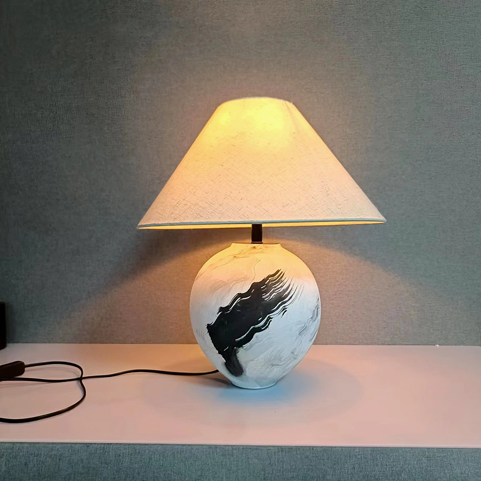 Off-white linen shade table lamp with artistic ceramic base illuminated on minimalist surface