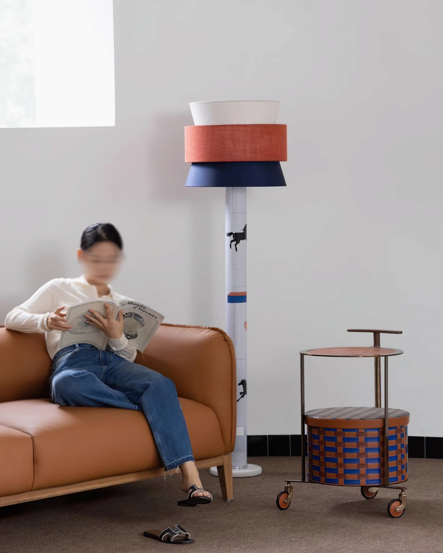 Statement floor lamp next to leather sofa in modern living room, woman reading magazine barefoot relaxed setting