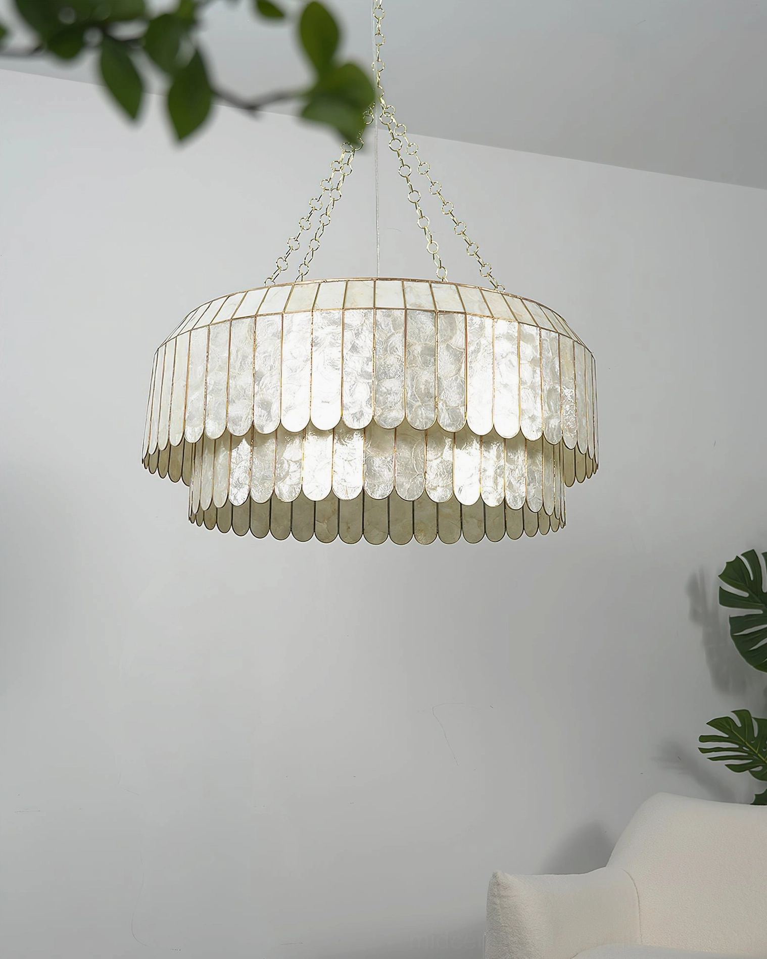 Aurelia capiz pendant lamp in minimalist living room with white sofa and green foliage, creating soft ambient coastal modern lighting