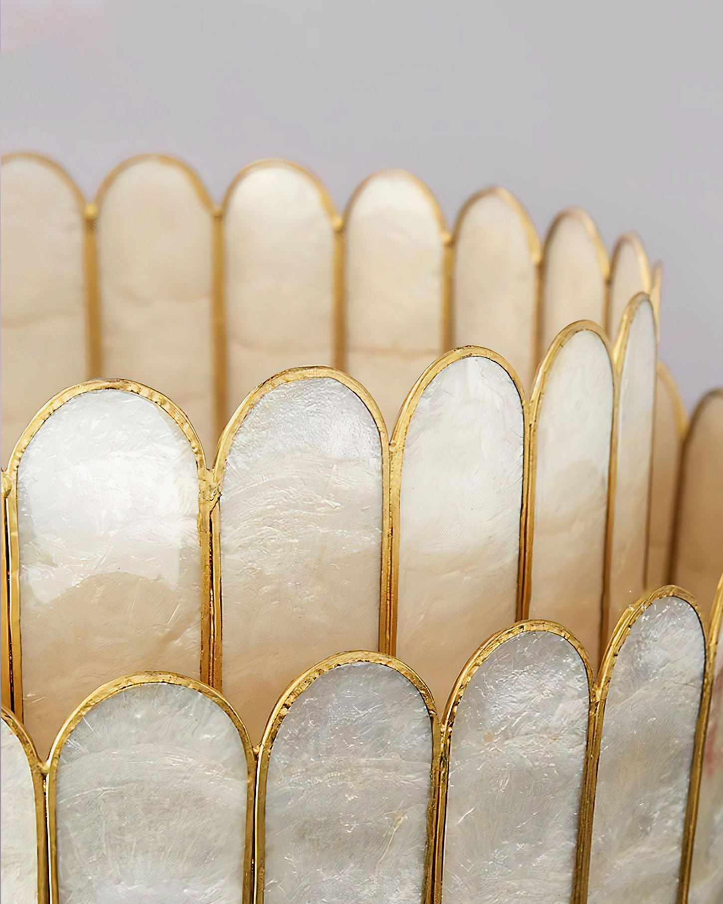 Close-up macro detail of hand-cut capiz shell panels showing scalloped edges, iridescent pearlescent texture, and gold metal framing