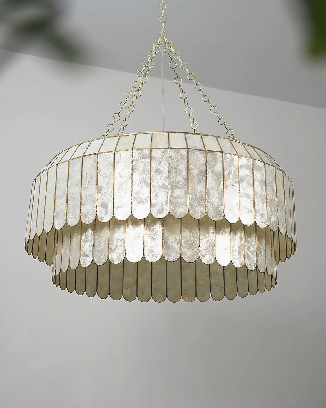 Aurelia capiz pendant lamp illuminated showing warm glow through translucent hand-cut shells, iridescent pearlescent effect in ambient lighting