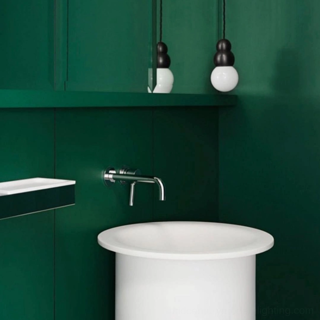 Pair of modern ball pendant lights with black metal tops and frosted spherical bulbs in green tiled bathroom