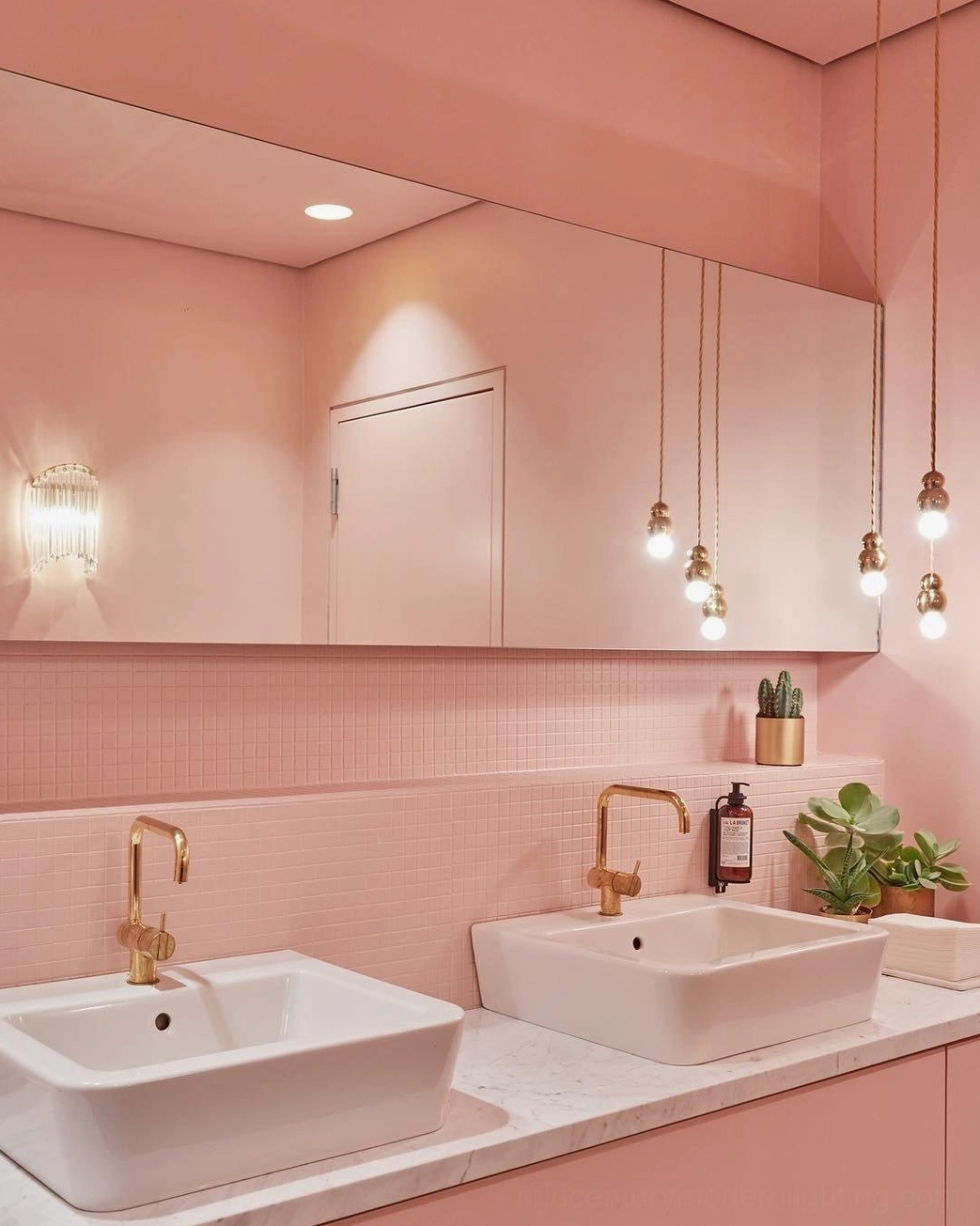 Multiple matching ball pendant lights in pink luxury dual-sink bathroom with gold faucets and warm interior