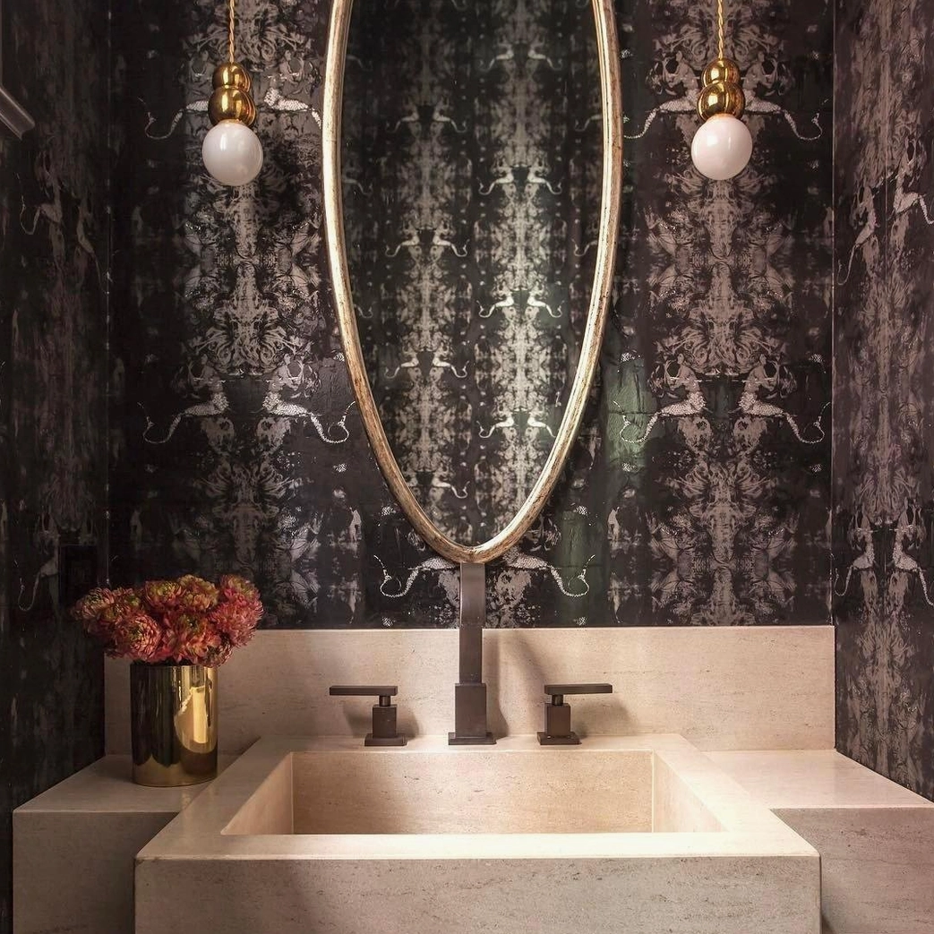 Twin ball pendant lights in vintage marble bathroom with oval gold mirror and floral vase decor
