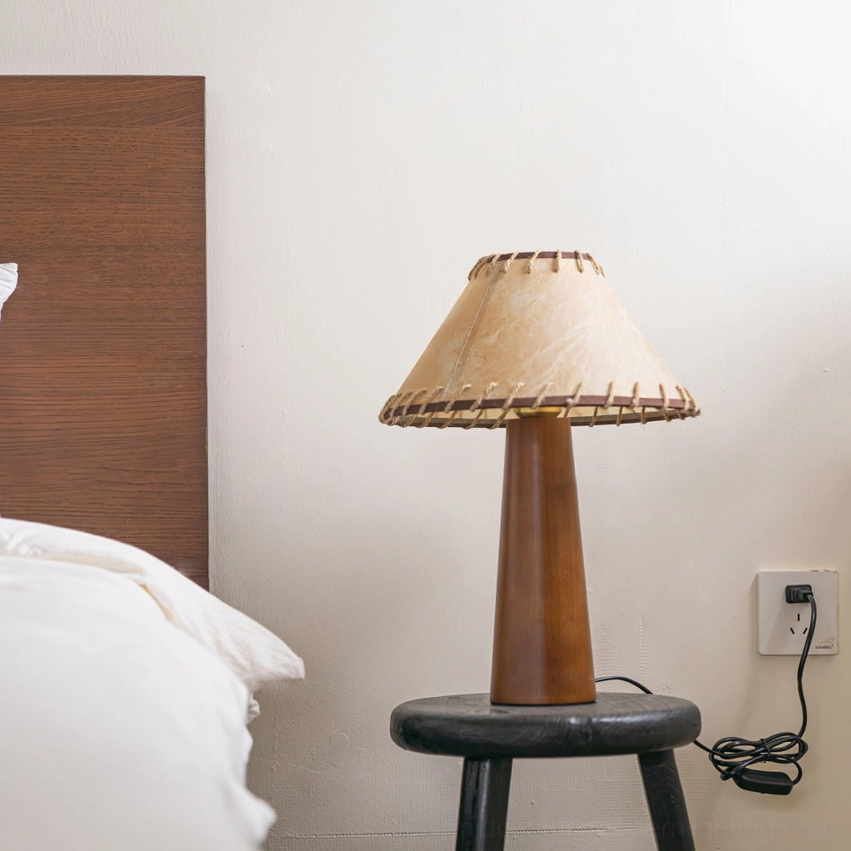Basica table lamp on black stool in bedroom corner showing electrical cord and power connection