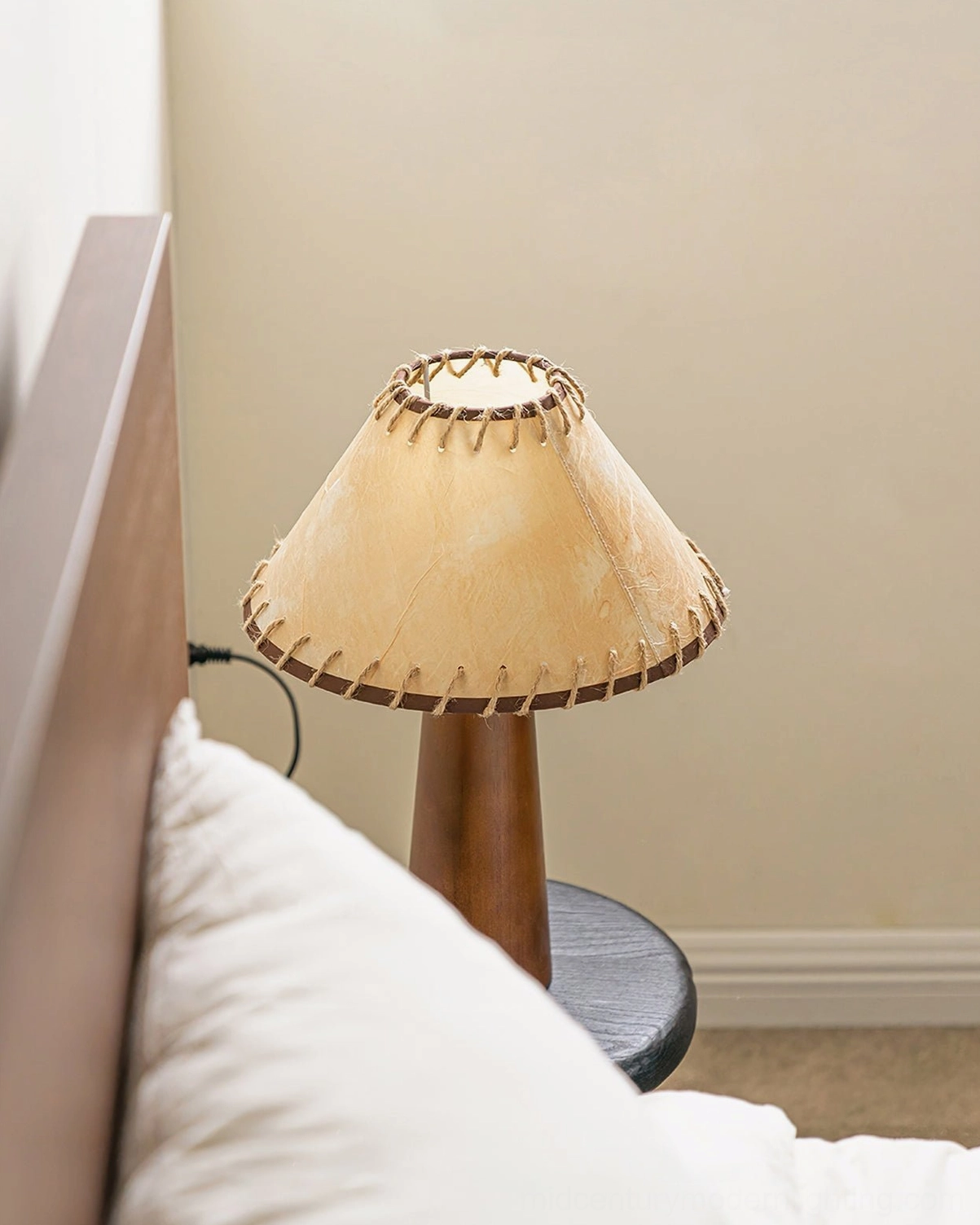 Basica mid-century modern table lamp on round side table in cozy bedroom environment