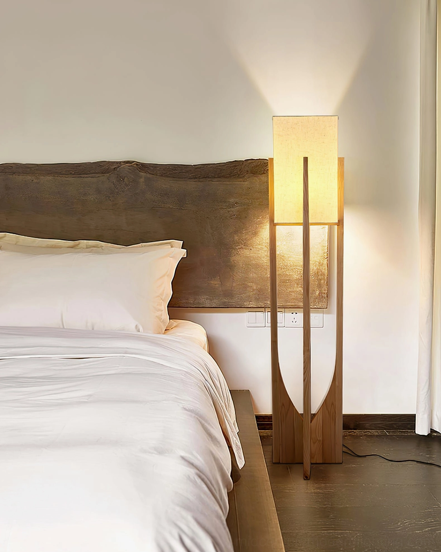 Wooden floor lamp creating warm glow in bedroom corner with bed and wooden headboard