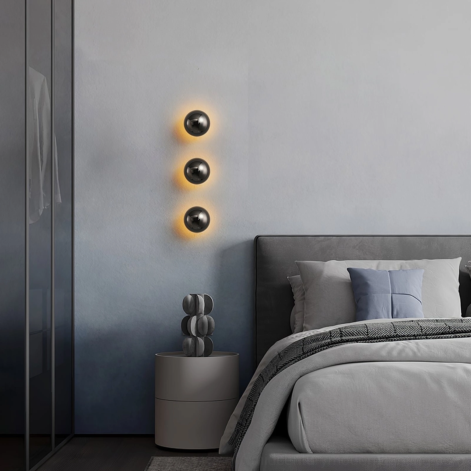 Set of three chrome sphere wall sconces in bedroom creating warm ambient lighting over headboard