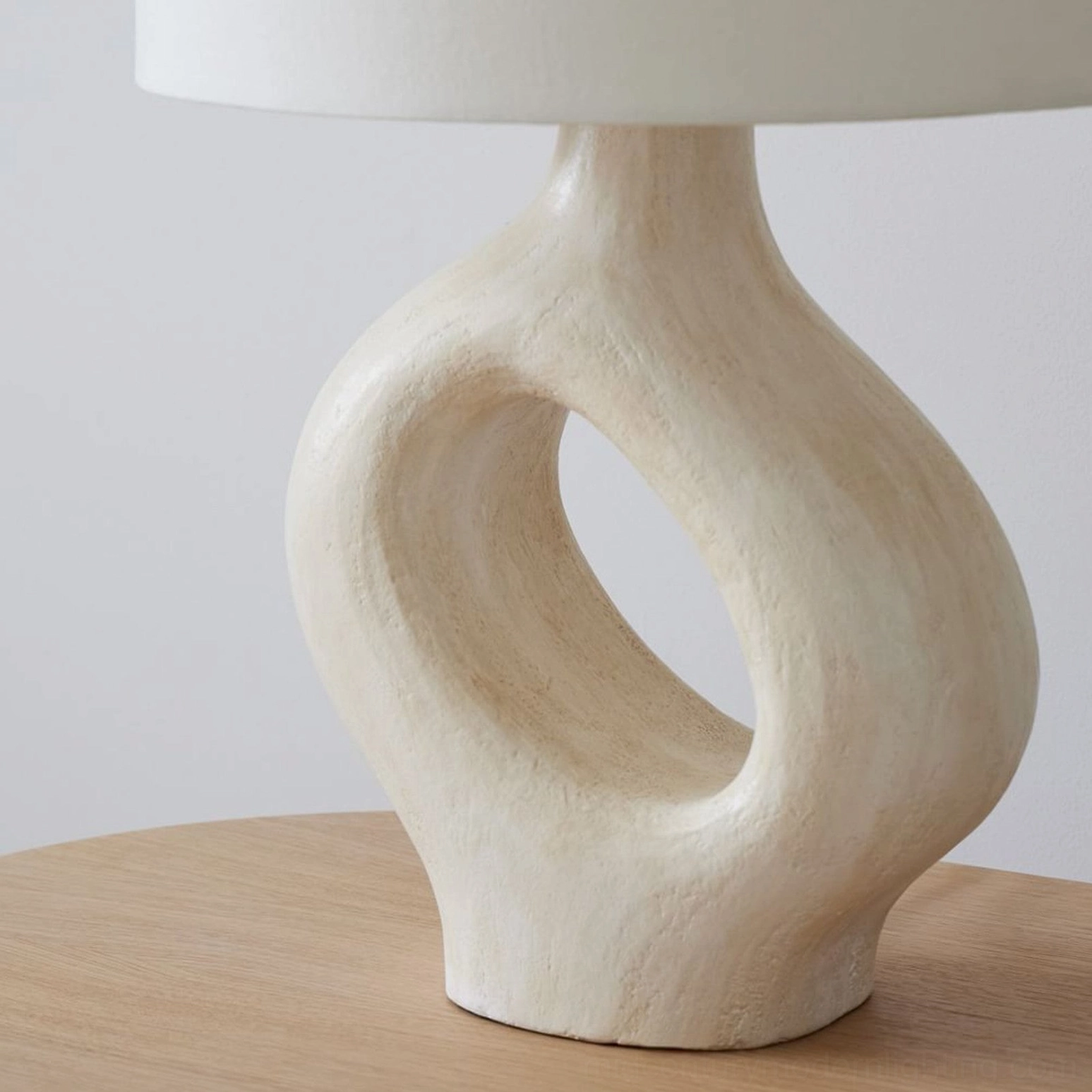Light beige hollow resin table lamp with curved organic ceramic base and matte finish on wooden side table