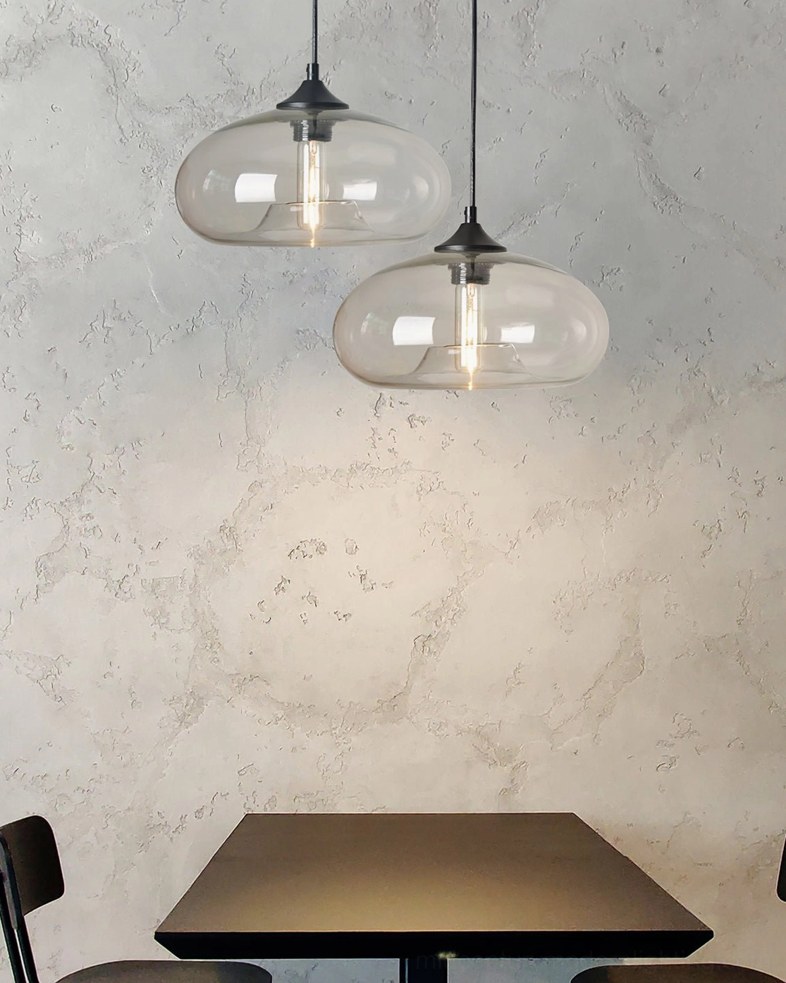 Pair of Bella clear glass pendant lights above dark wood dining table with marble wall, modern minimalist dining