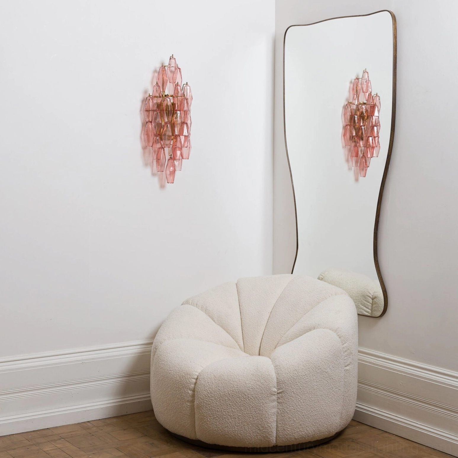 Light pink polyhedral glass wall sconce in contemporary living space with curved floor mirror and minimalist furniture