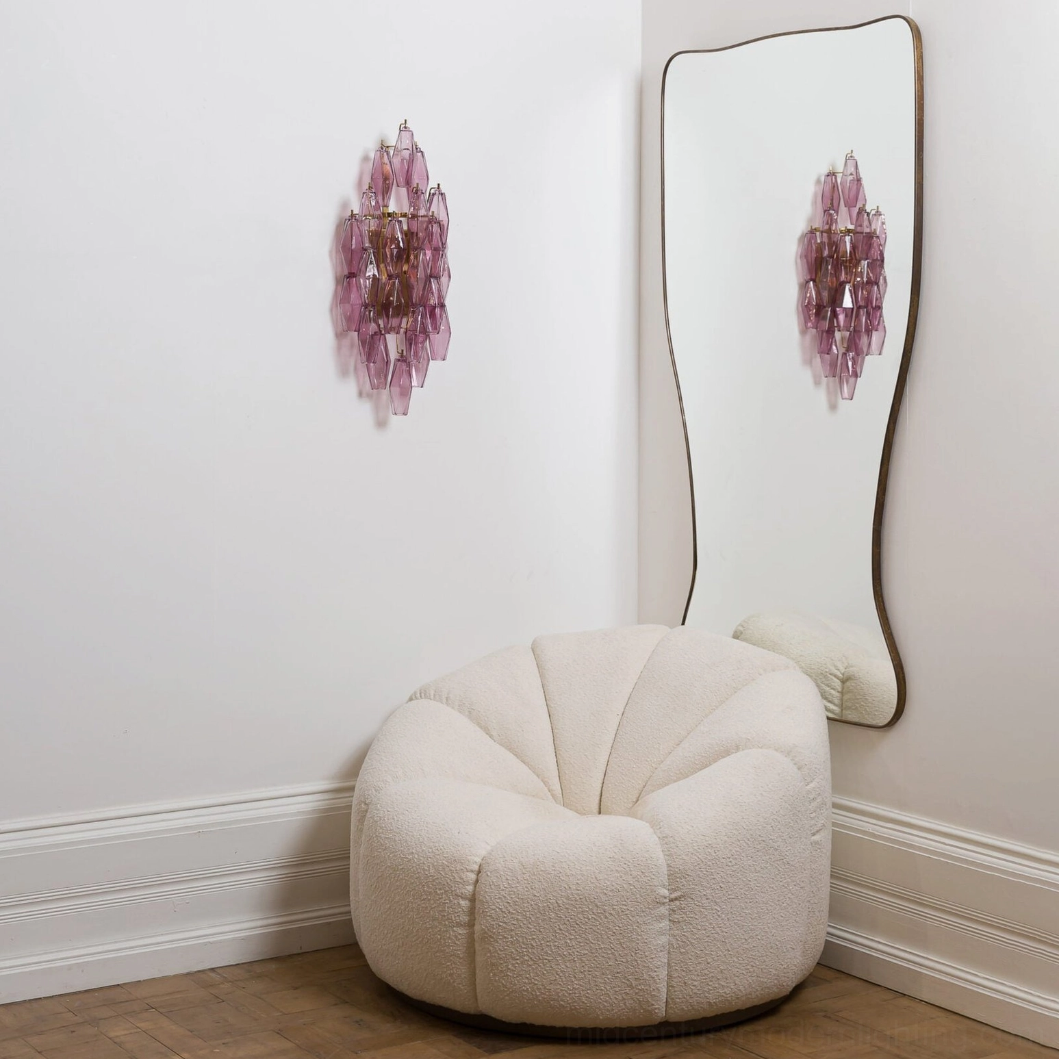 Deep purple-pink polyhedral glass sconce with gold accents in contemporary interior with curved mirror