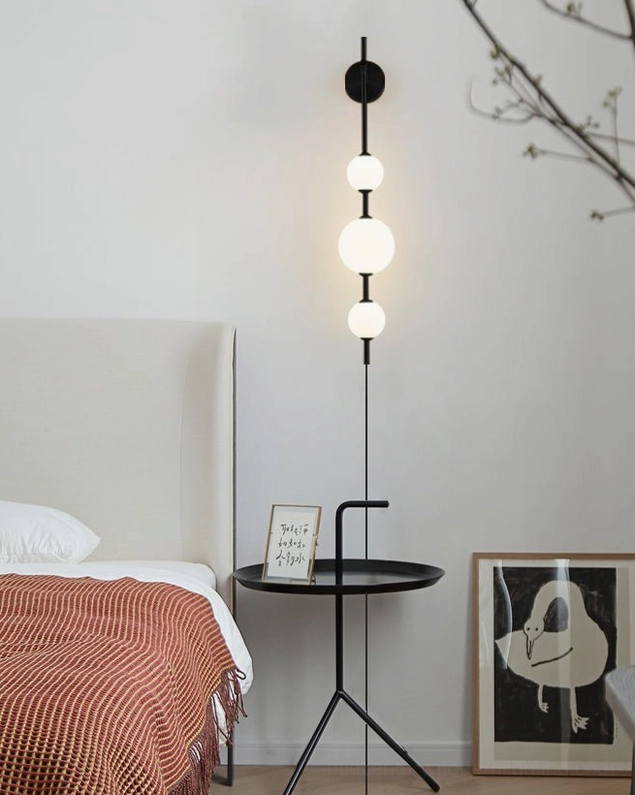 Matte black vertical globe wall sconce with three frosted glass orbs in minimalist bedroom design