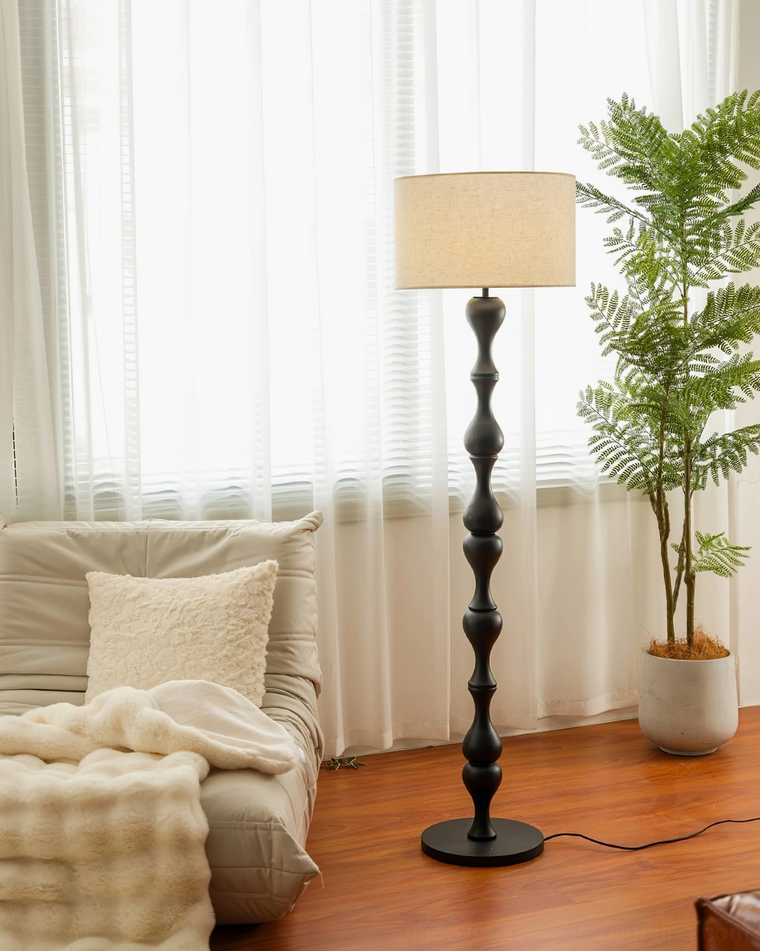 Black Norden standing lamp in cozy living room with sofa and potted plant, vintage home decor