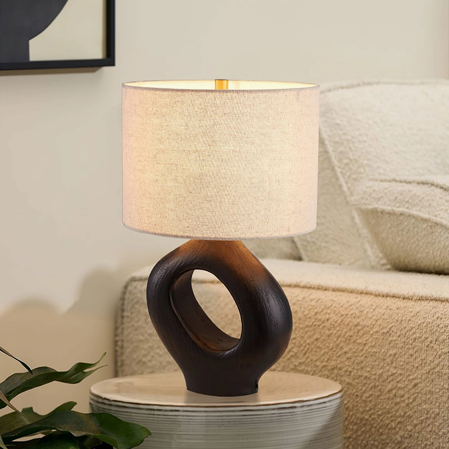 Dark brown ceramic Sauce table lamp on striped round side table next to contemporary boucle sofa