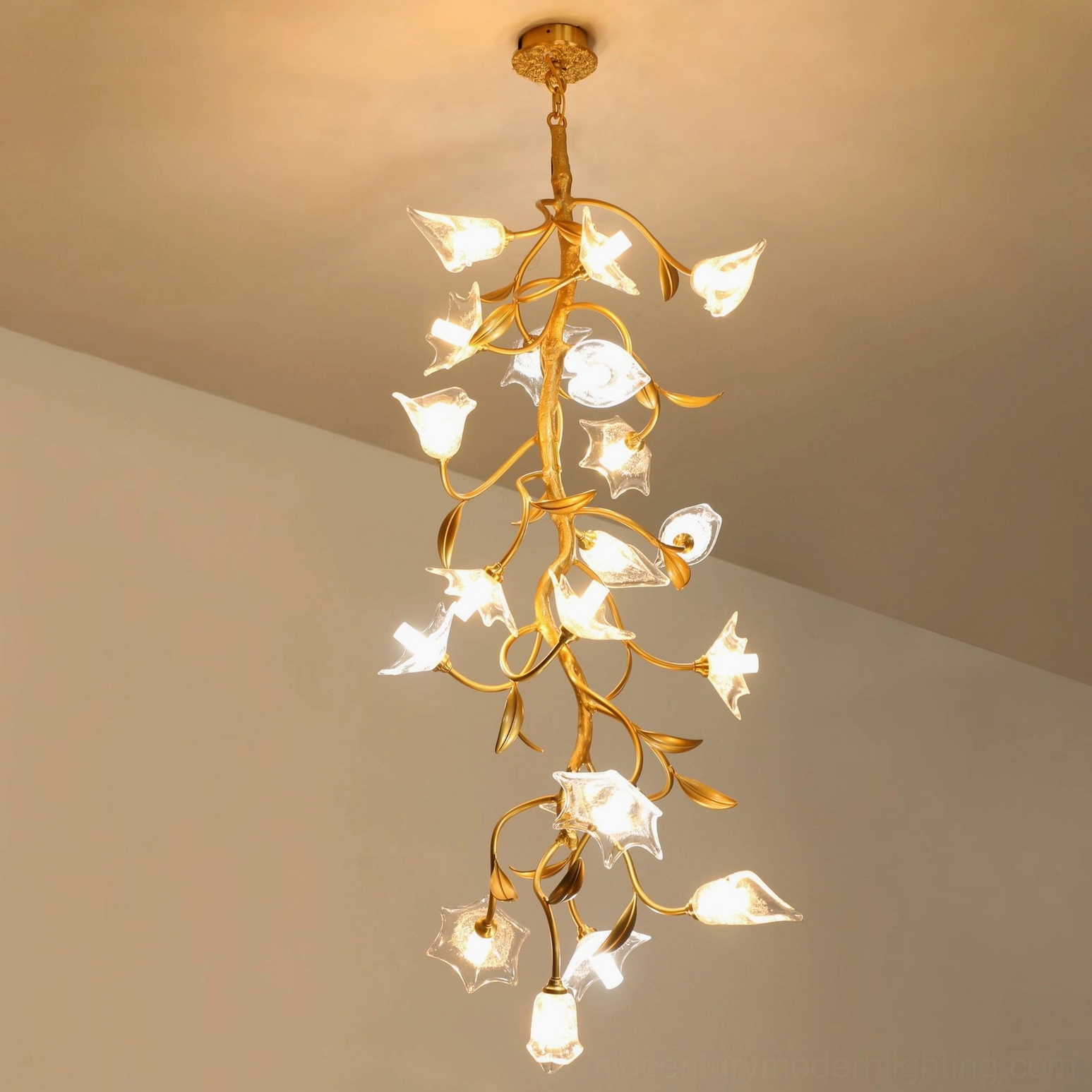 Modern botanical chandelier lit with warm LED light, winding gold branches with delicate glass flowers in living room setting