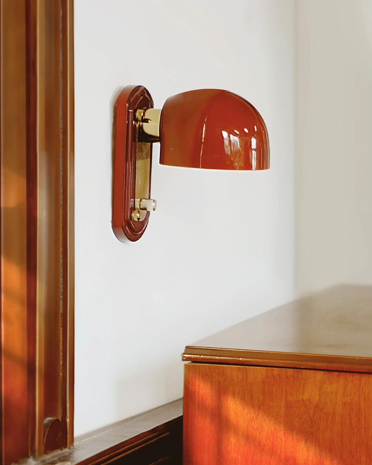Bradley retro wall-mounted light fixture with deep red dome shade and brass hardware displayed in wood-paneled interior