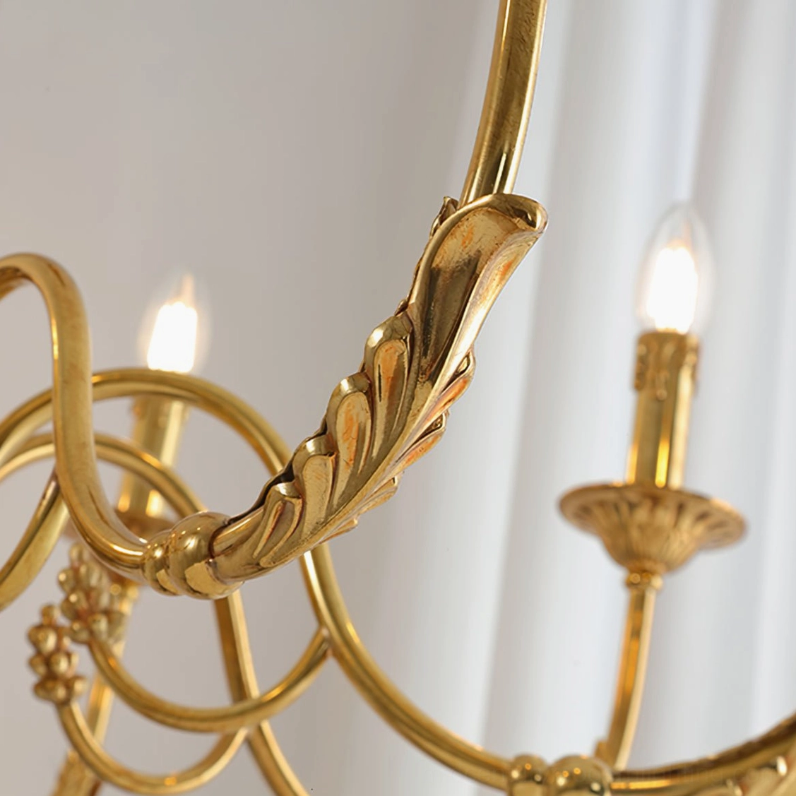 Side view of brass chandelier frame showing lit candle bulbs and leaf-carved details
