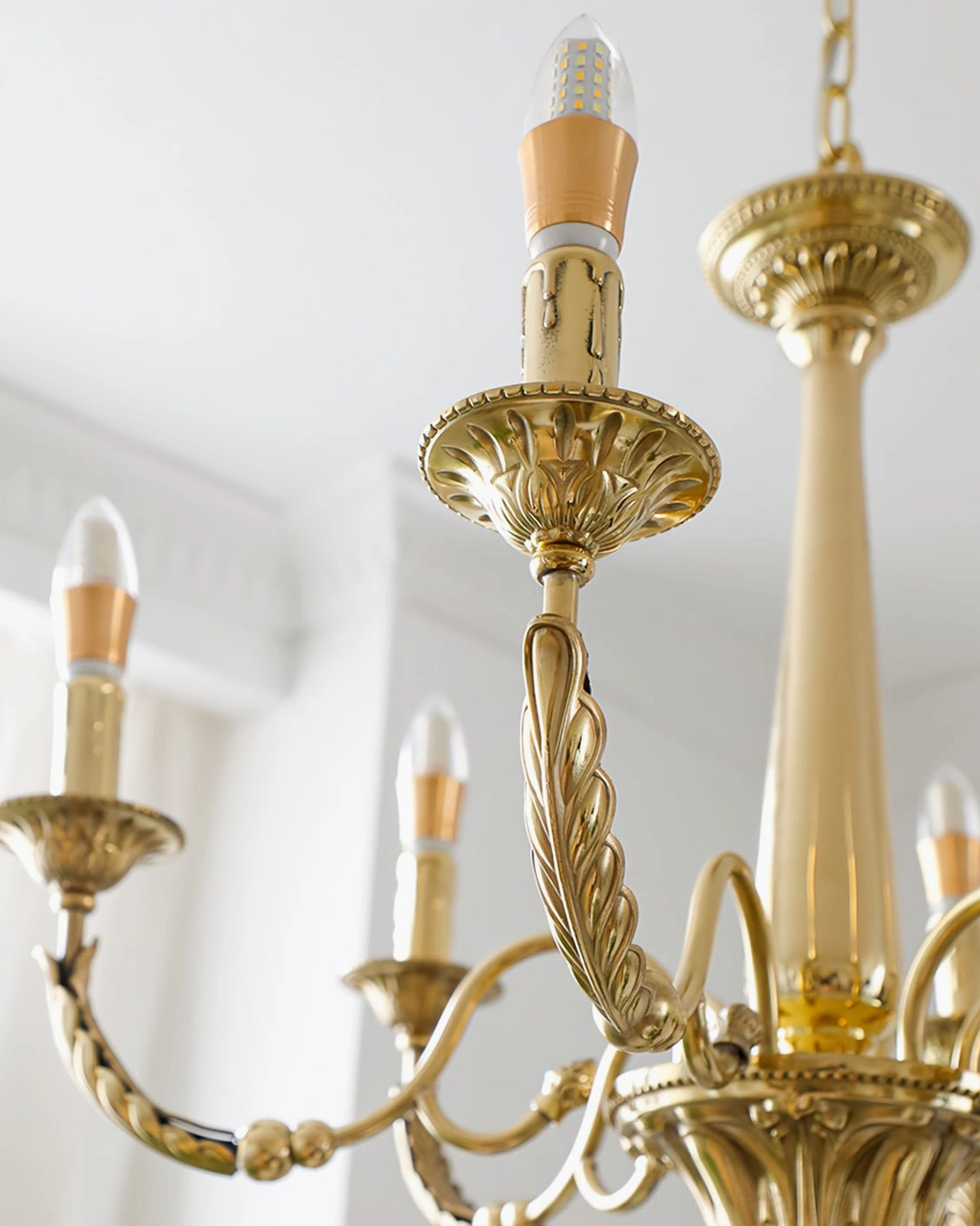 Three-quarter view of brass candle chandelier featuring leaf-shaped carvings and lit bulbs in white room