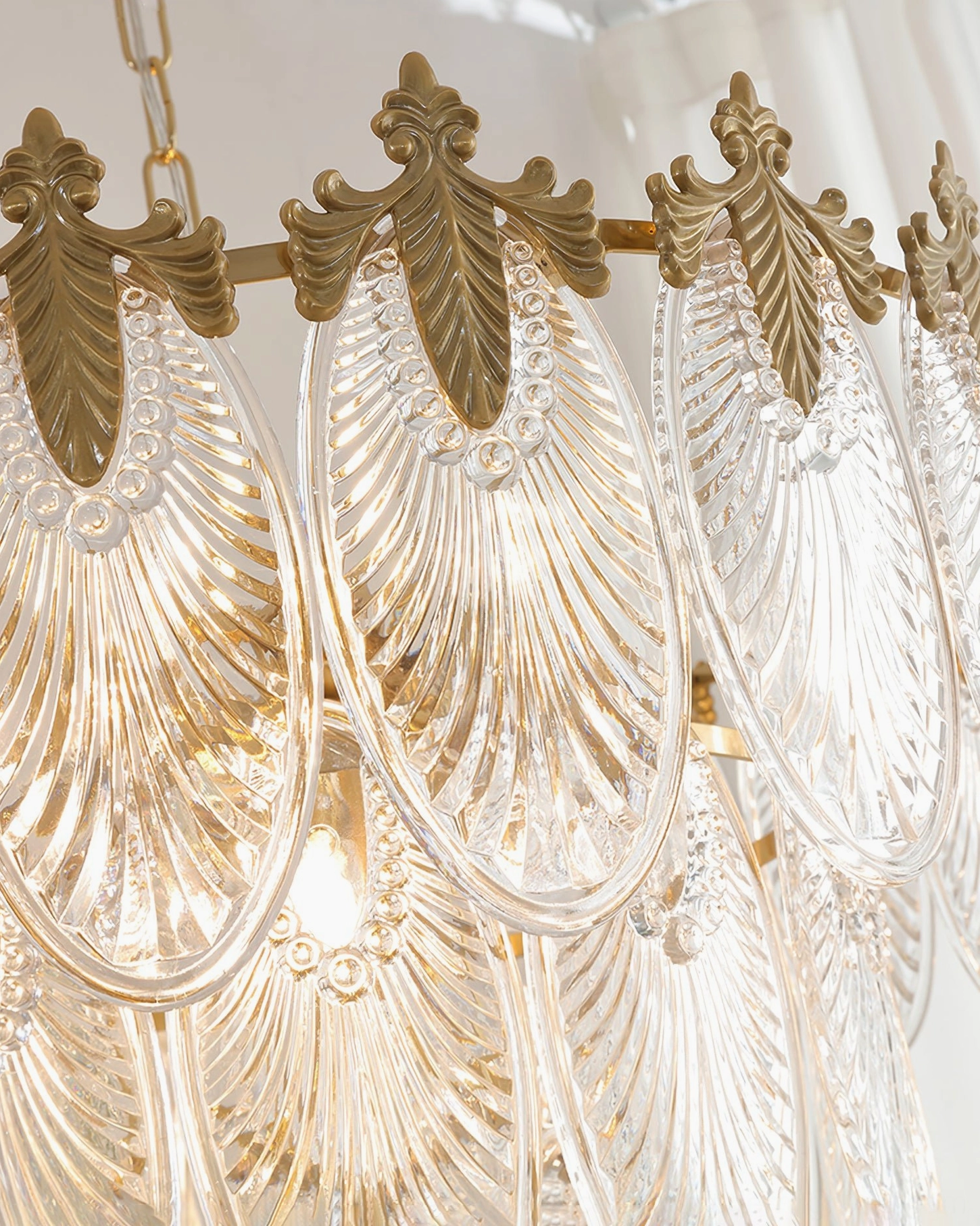 Close-up detail of brass leaves chandelier showing fluted carved glass palmette leaf pendants and brass acanthus-leaf crown mounting