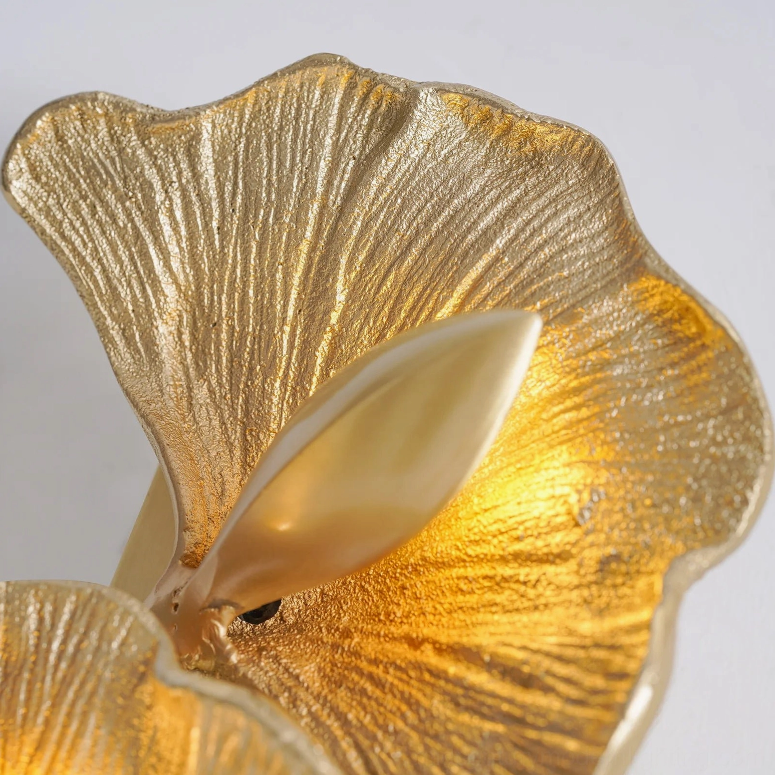 Side close-up of brass ginkgo leaf wall lamp highlighting brushed metallic surface and craftsmanship