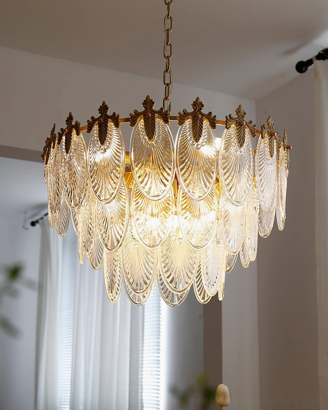 Lighted three-ring brass chandelier with acanthus leaf crowns and fluted glass tiers suspended in interior room with sheer window
