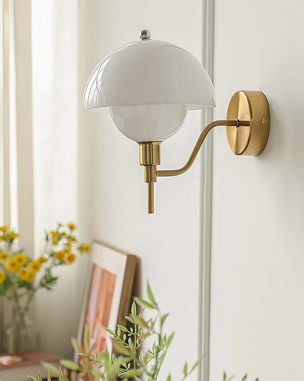 Brass anchored orb wall lamp in beige glass installed in cozy home corner with sheer curtains and artwork