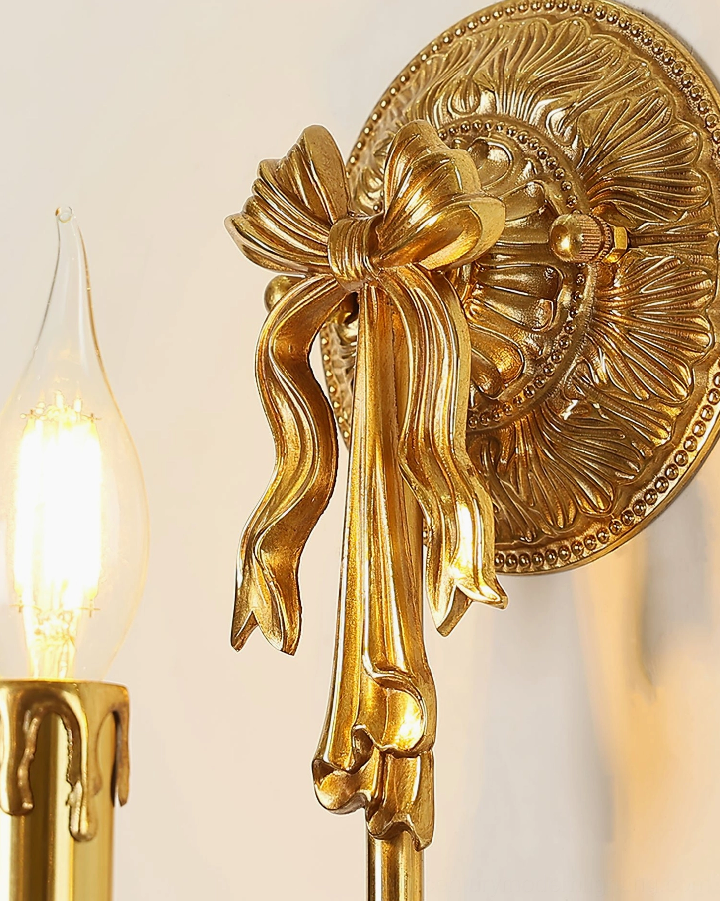 Close-up of brass wall sconce showing carved floral base and ribbon bow embellishment
