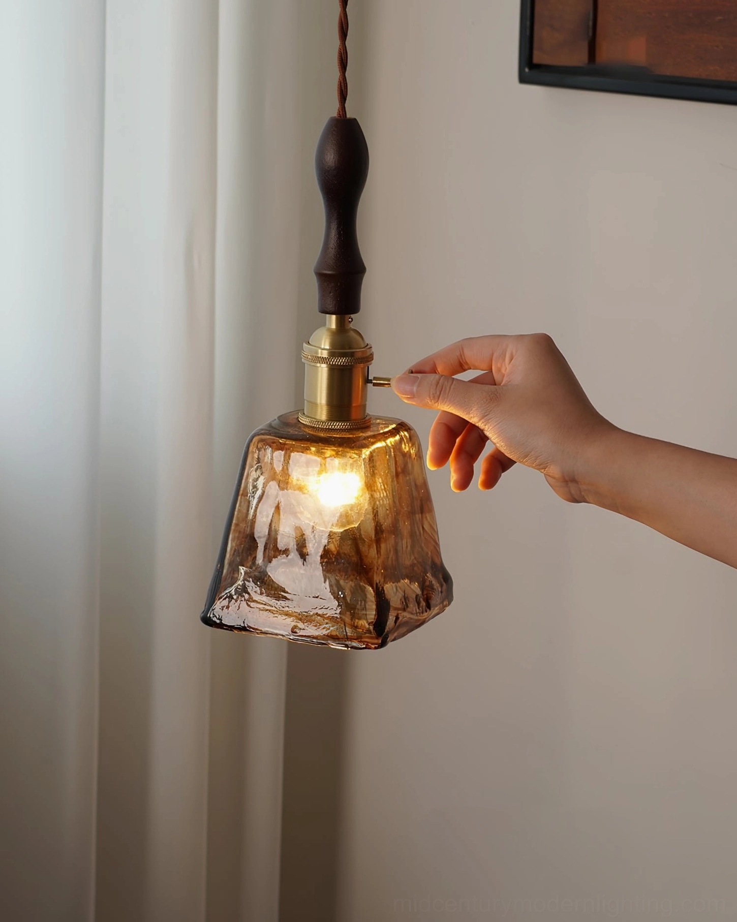Hand adjusting brass switch on marbled amber glass pendant lamp, warm Edison bulb visible, interior detail shot