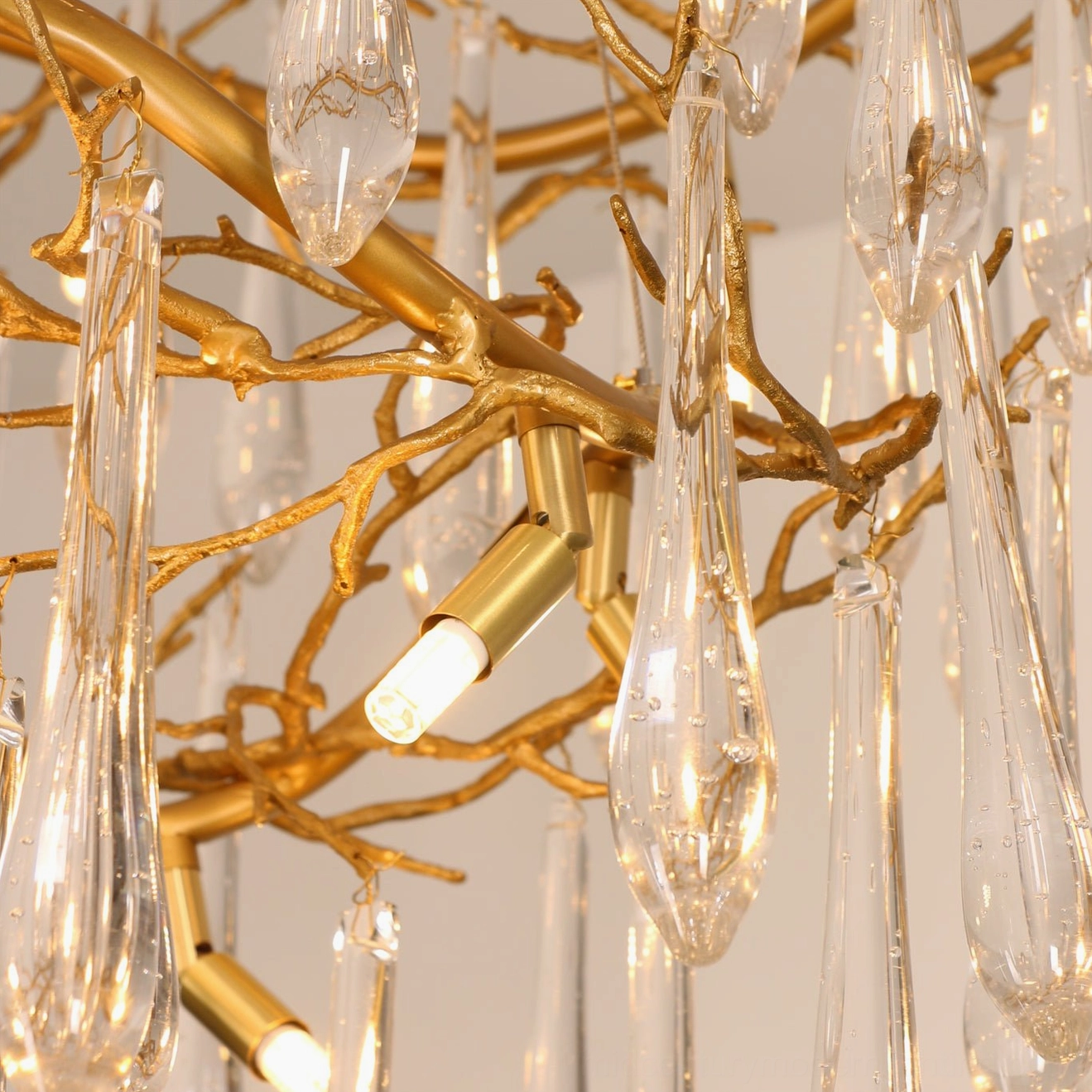 Close-up side view of brass waterfall chandelier showing gold metal branches, clear teardrop glass pendants, and exposed G9 bulb sockets