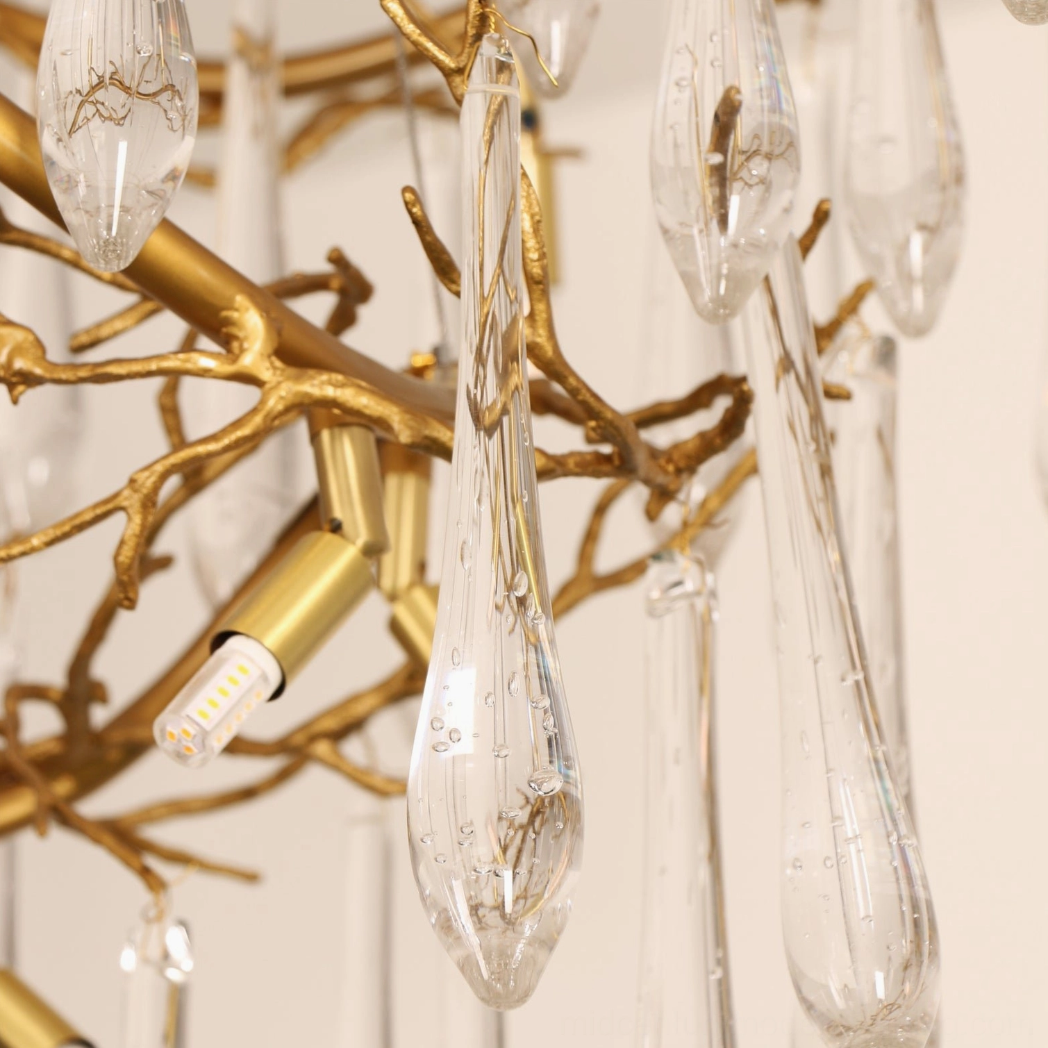 Macro detail of brass waterfall chandelier crystal glass teardrop pendants with subtle internal light-catching bubbles and polished gold branch framework
