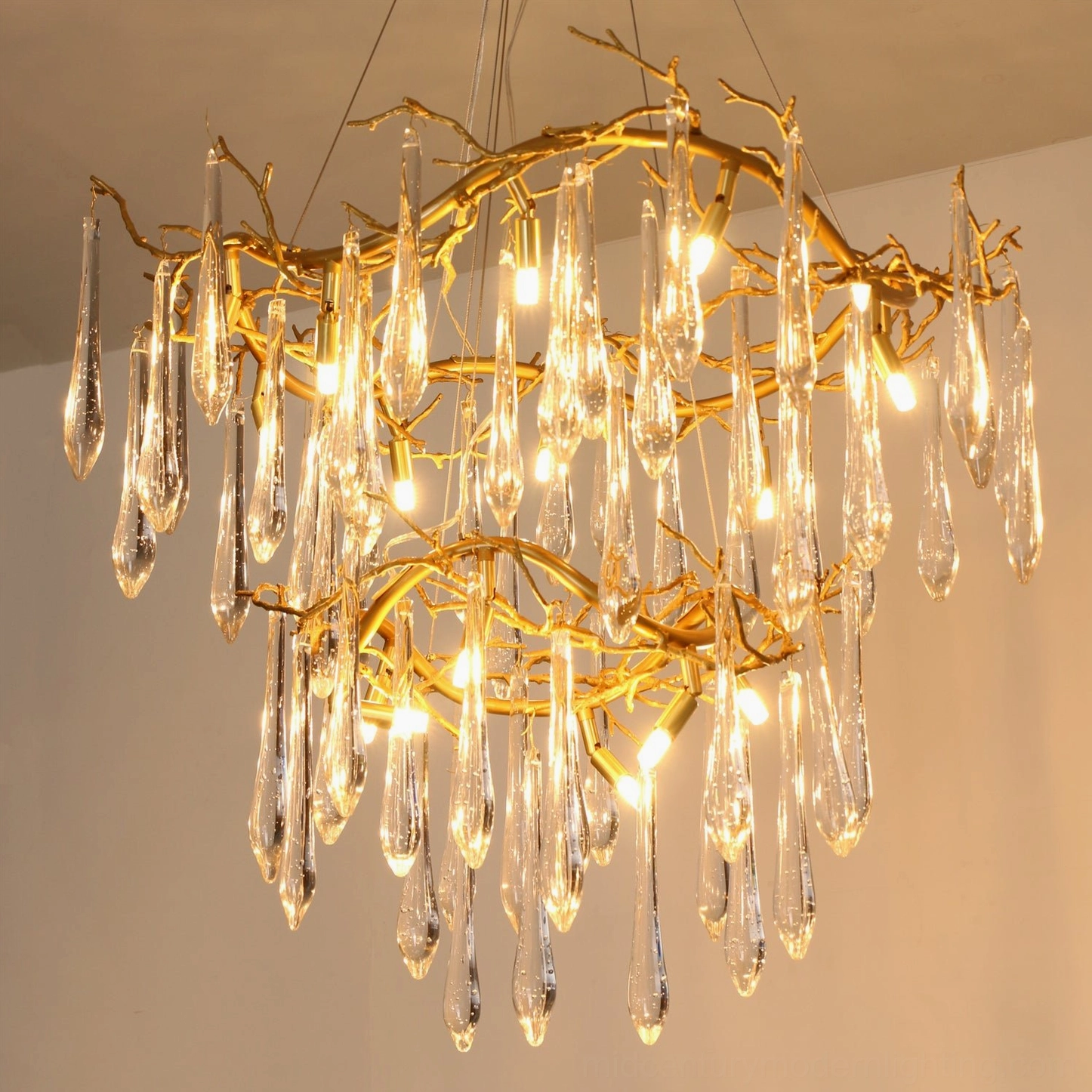 Illuminated brass waterfall chandelier with glowing filament-style bulbs, double-tier gold branch frame close-up against ceiling background